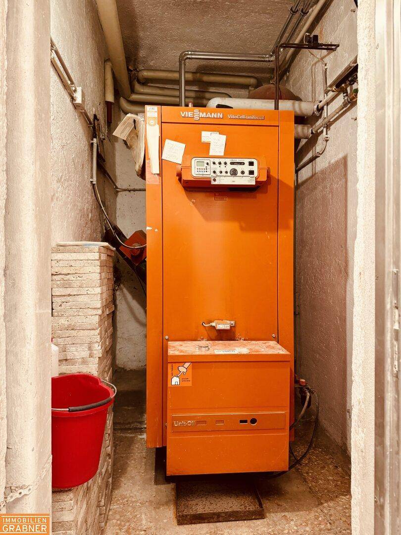 Heizungsraum mit einem großen orangefarbenen Heizkessel und Rohren.