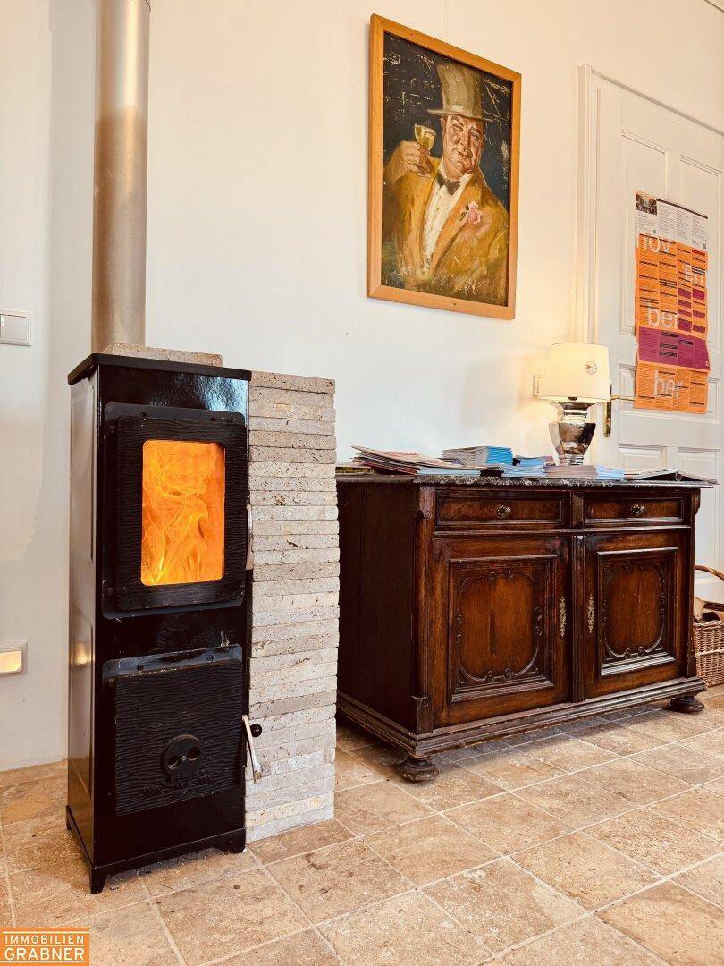 Kaminofen mit Steinverkleidung und antiker Holzkommode in einem hellen Raum.