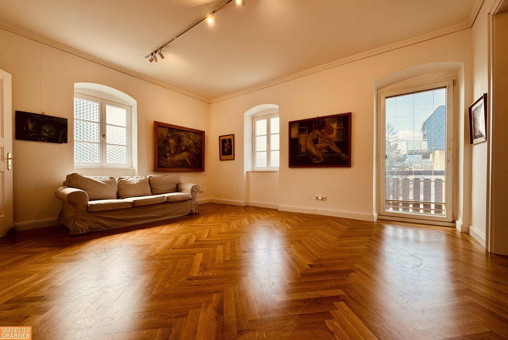 Heller Wohnraum mit Fischgrätparkett, Sofa und Zugang zu einem französischen Balkon.