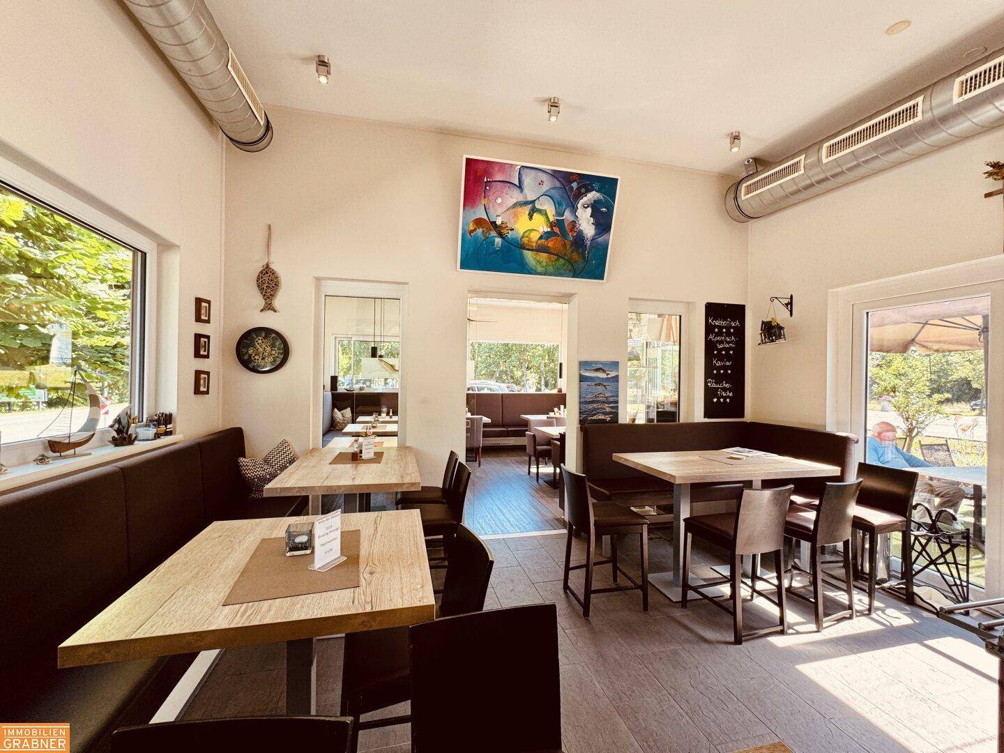 Geräumiger Restaurantbereich mit verschiedenen Sitzgelegenheiten, Kunstwerken und sichtbaren Lüftungsrohren an der Decke.