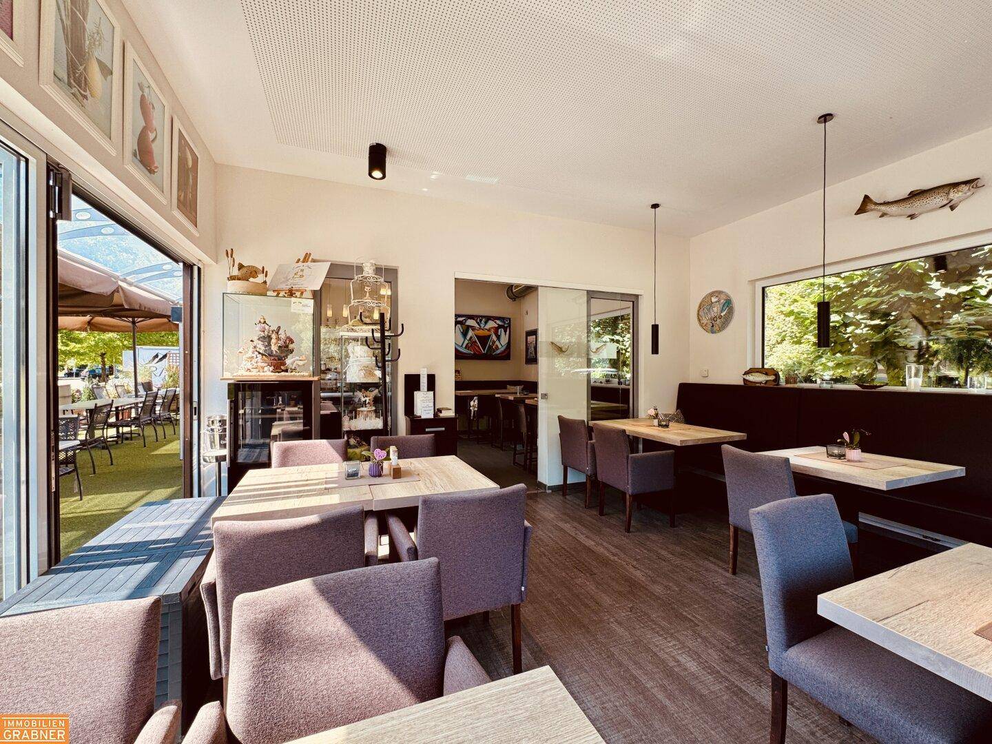 Innenansicht des Restaurants mit Blick auf den Außenbereich durch große Glastüren, die zum Essen im Freien einladen.