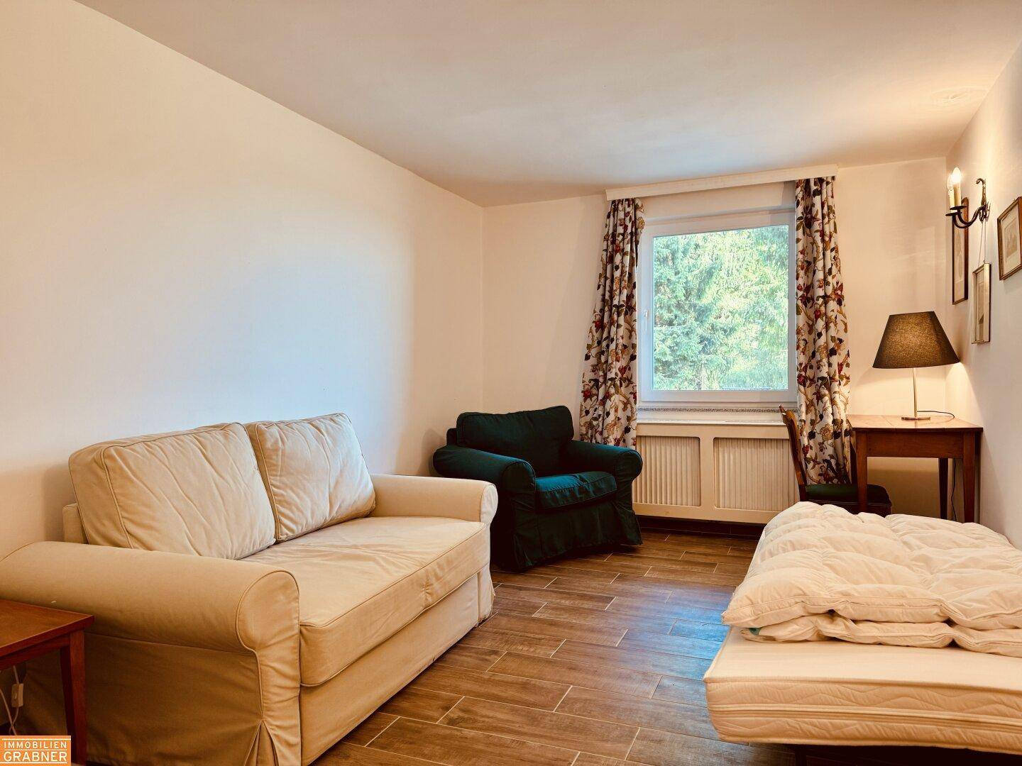Einfaches Schlafzimmer oder Gästezimmer mit Sofa, Einzelbett und Blick ins Grüne.