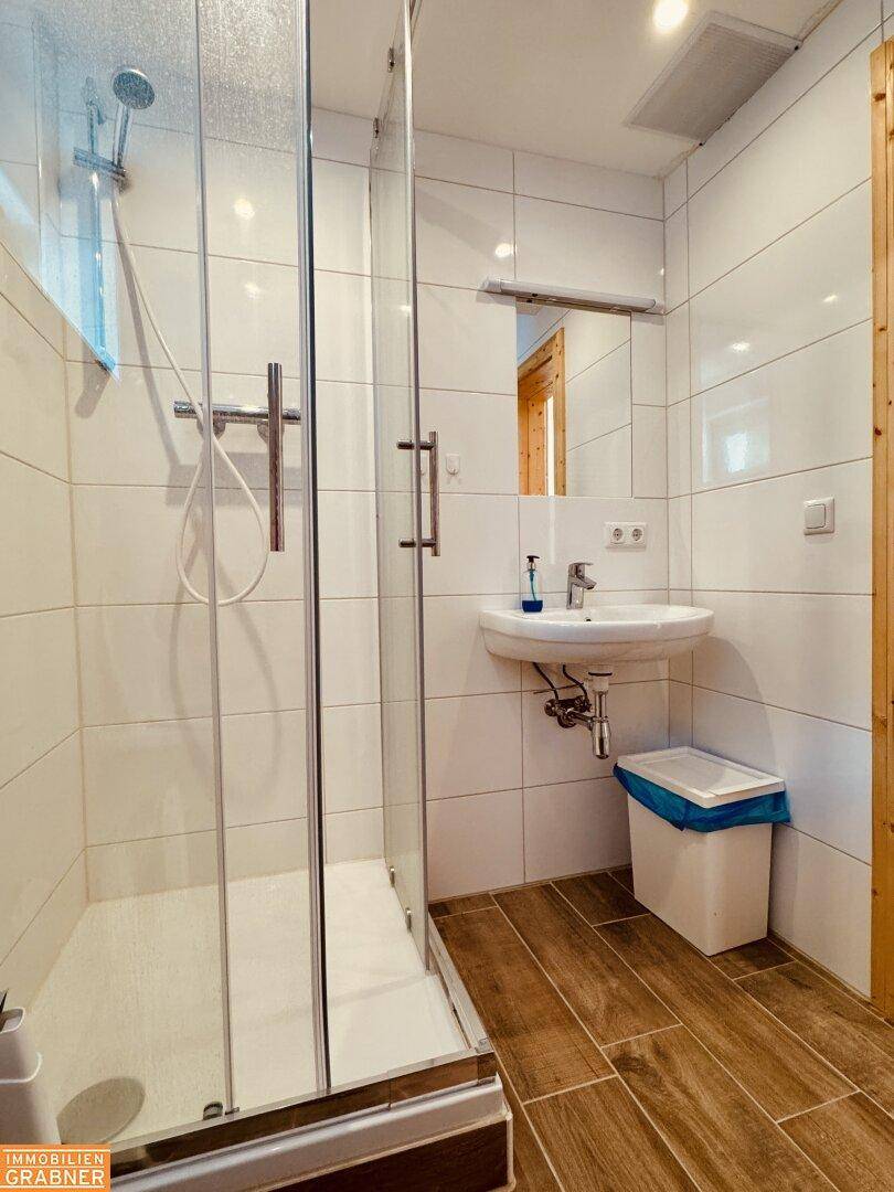 Modernes Badezimmer mit Duschkabine, Waschbecken und weißen Fliesen.