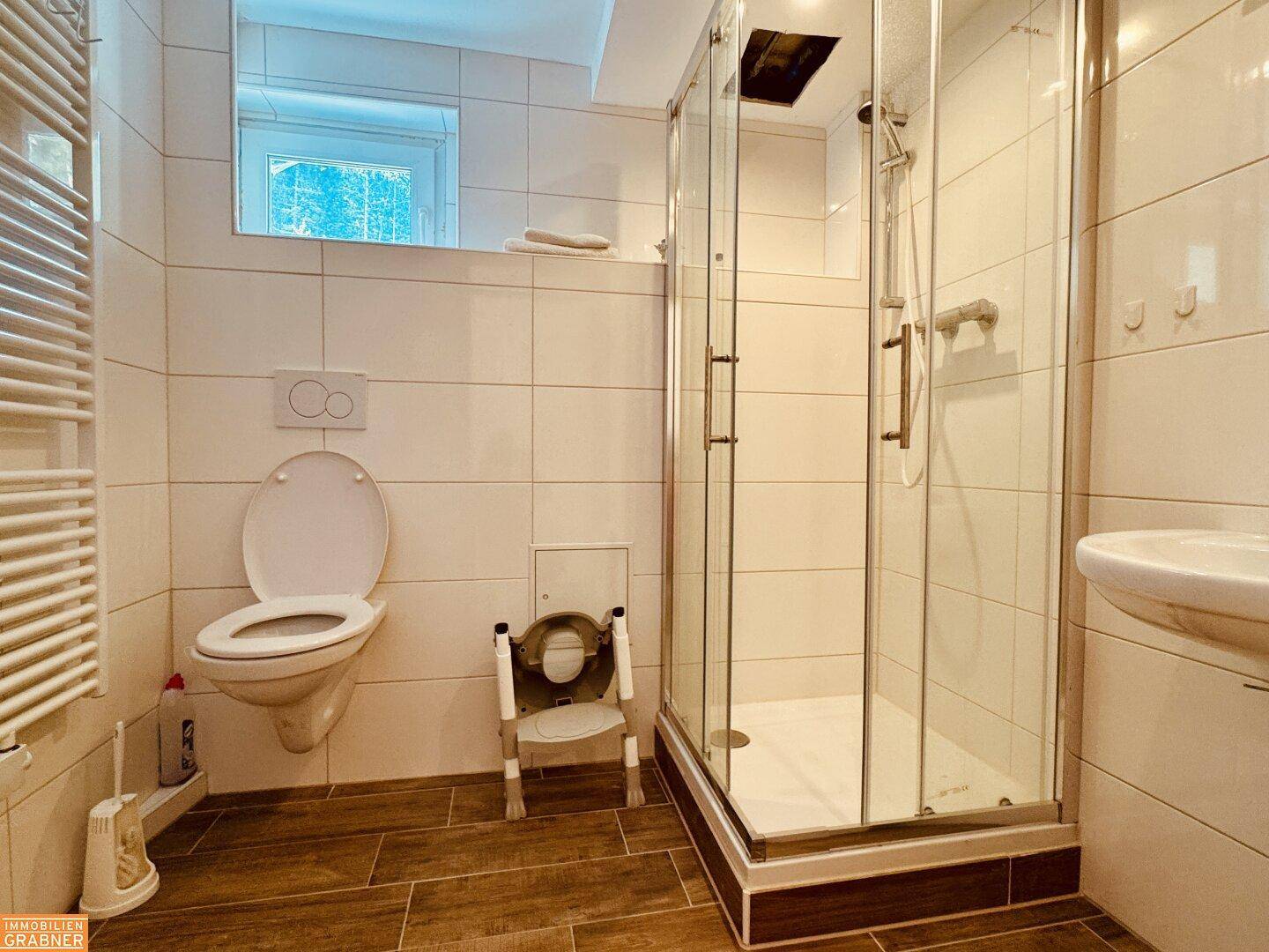 Badezimmer mit WC, Duschkabine und Waschbecken, ausgestattet mit Haltegriffen für Barrierefreiheit.
