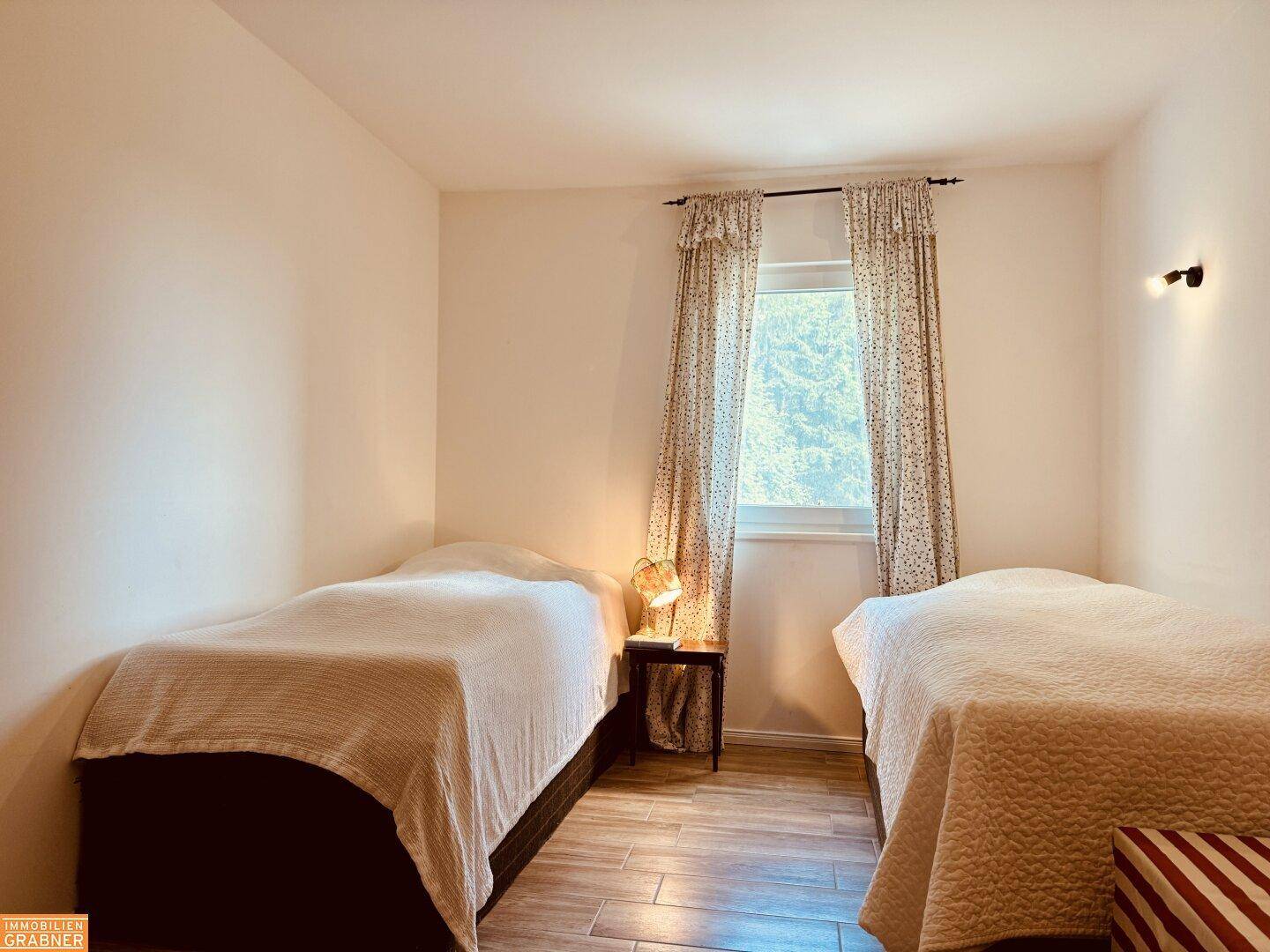 Schlafzimmer mit zwei Einzelbetten, Holzboden und Fenster mit Blick ins Grüne.