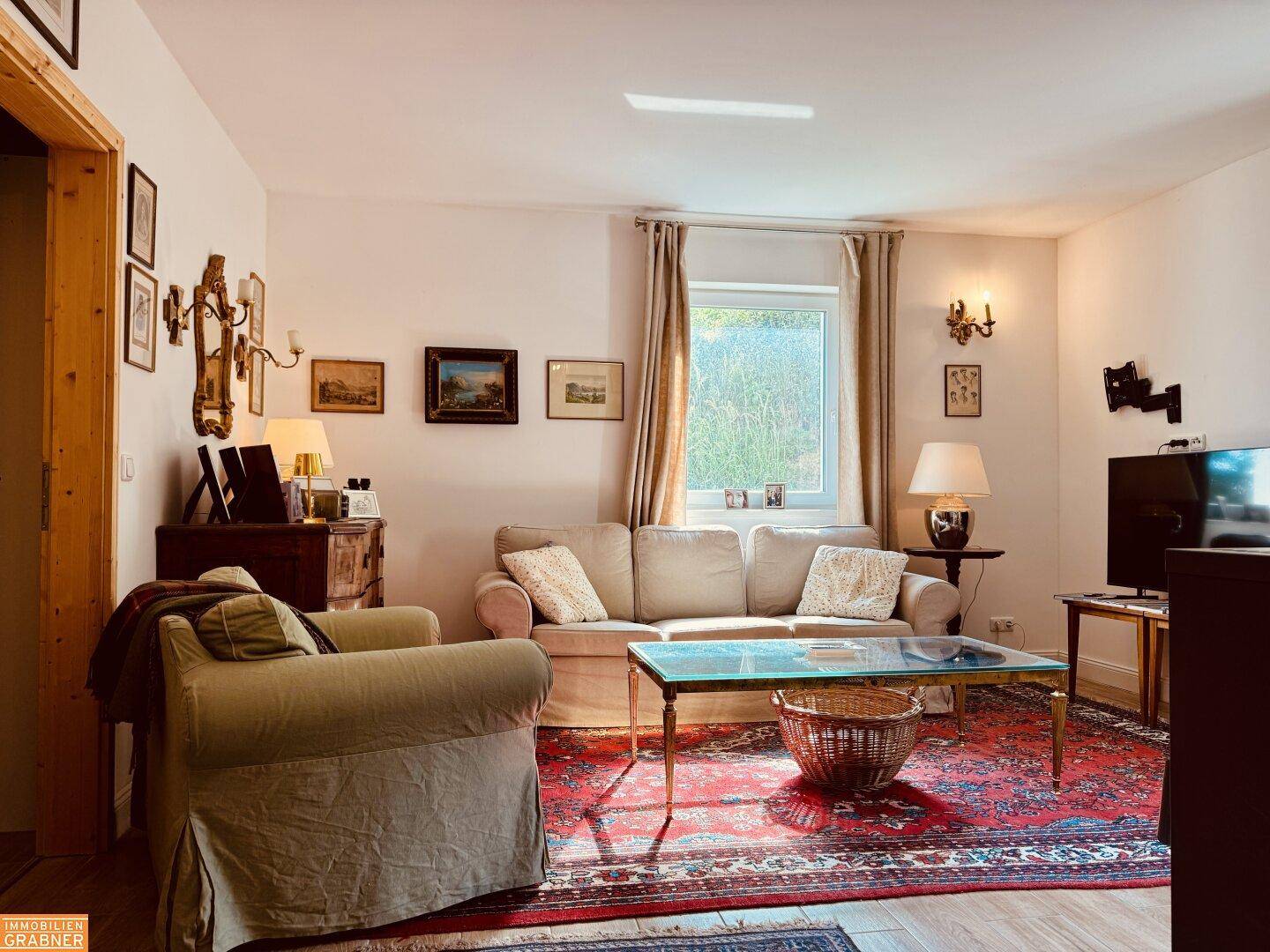 Wohnzimmer mit beigem Sofa, Teppich und Fenster, das viel natürliches Licht hereinlässt.