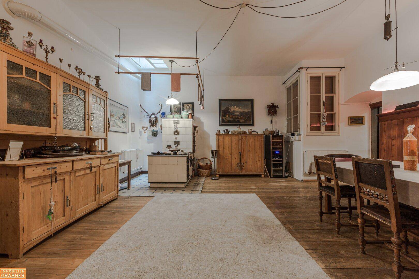 Geräumiger Wohn- und Essbereich mit Holzboden, traditionellem Kachelofen und rustikalen Holzmöbeln.