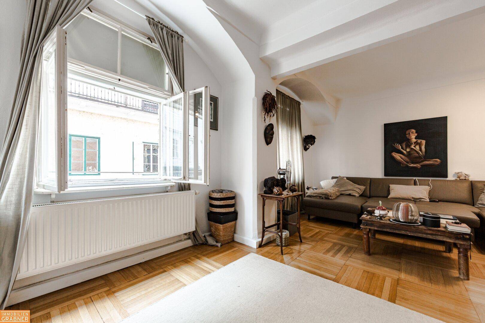 Helles Wohnzimmer mit großem Fenster, Heizkörper und Parkettboden.