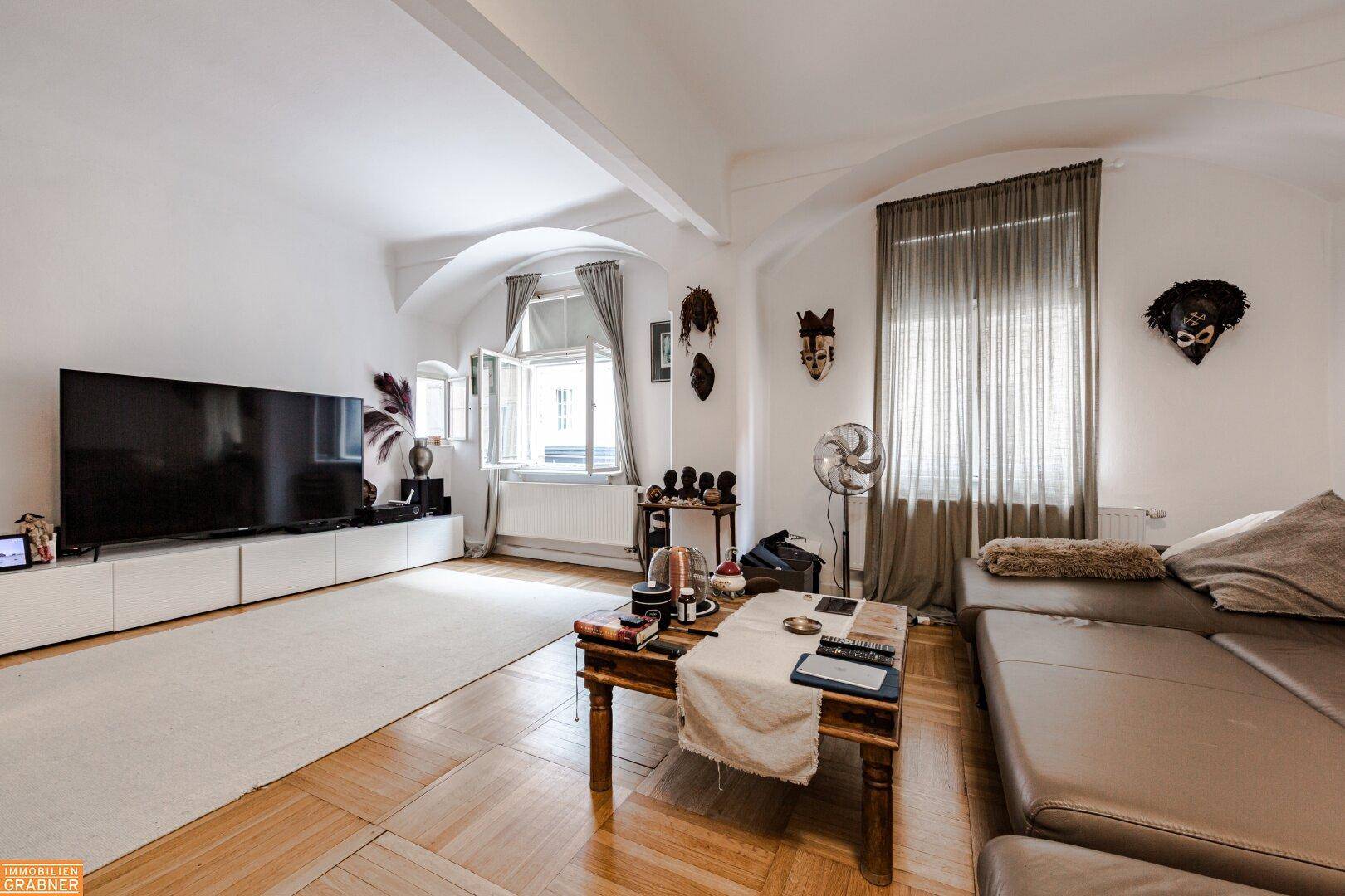 Helles Wohnzimmer mit großem Fernseher, modernem Sofa und Parkettboden.