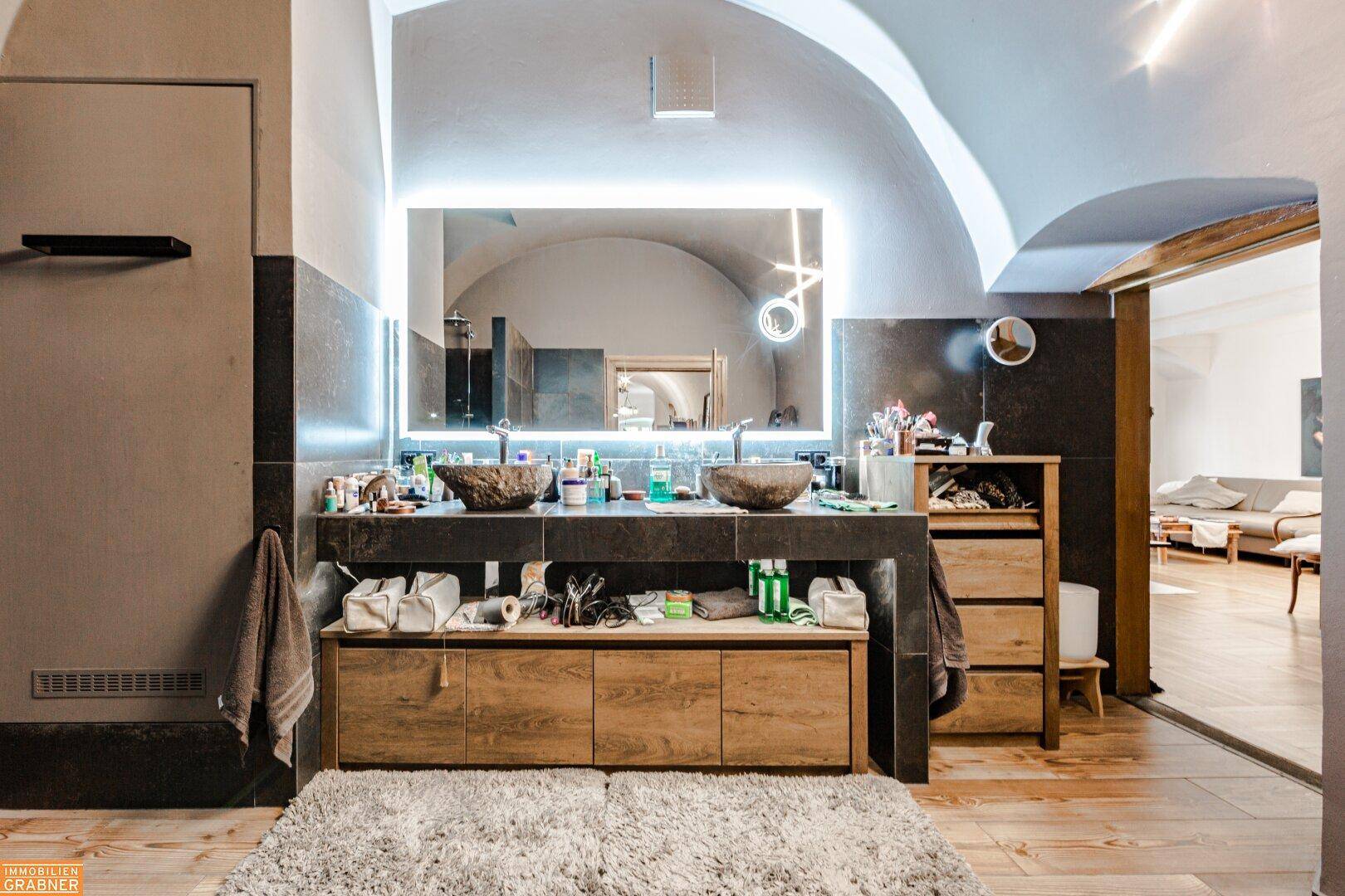 Modernes Badezimmer mit Doppelwaschbecken, beleuchtetem Spiegel und gewölbter Decke.