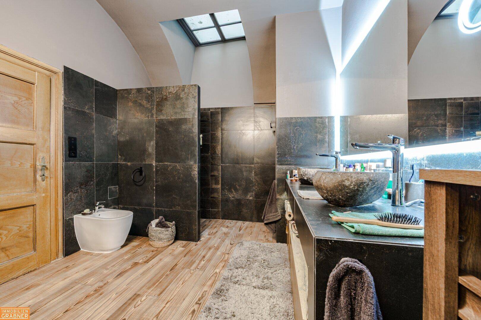 Modernes Badezimmer mit begehbarer Dusche, Bidet und dunklen Fliesen.