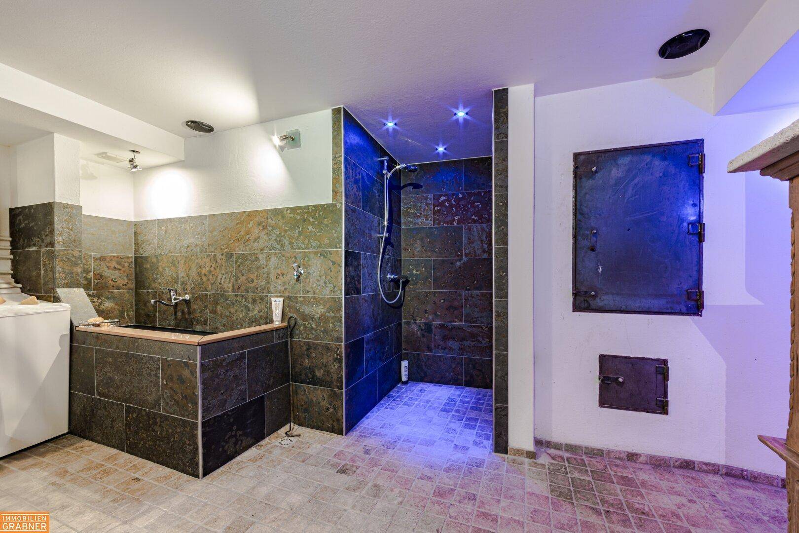 Spa-ähnlicher Bereich mit Badewanne, Dusche und dunklen Natursteinfliesen.