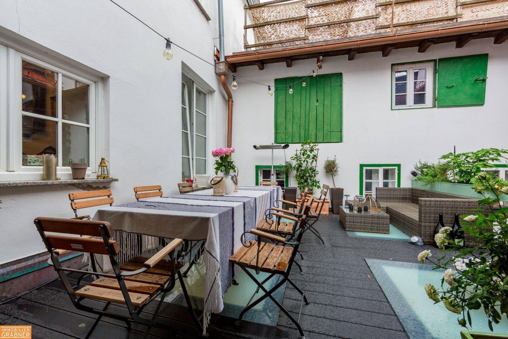 Gemütliche Terrasse mit Esstisch, Sitzgelegenheiten und Pflanzen in einem Innenhof.