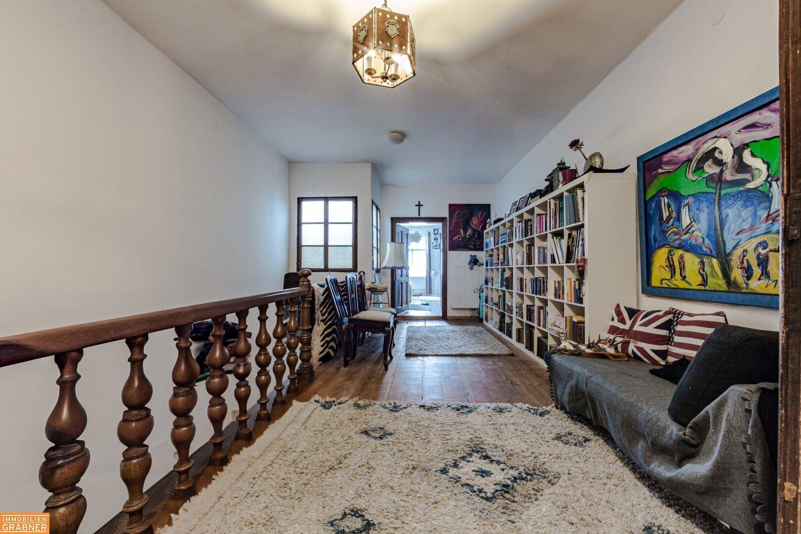 Heller Flur im Obergeschoss mit Bücherregal, Sofa und Holzgeländer.