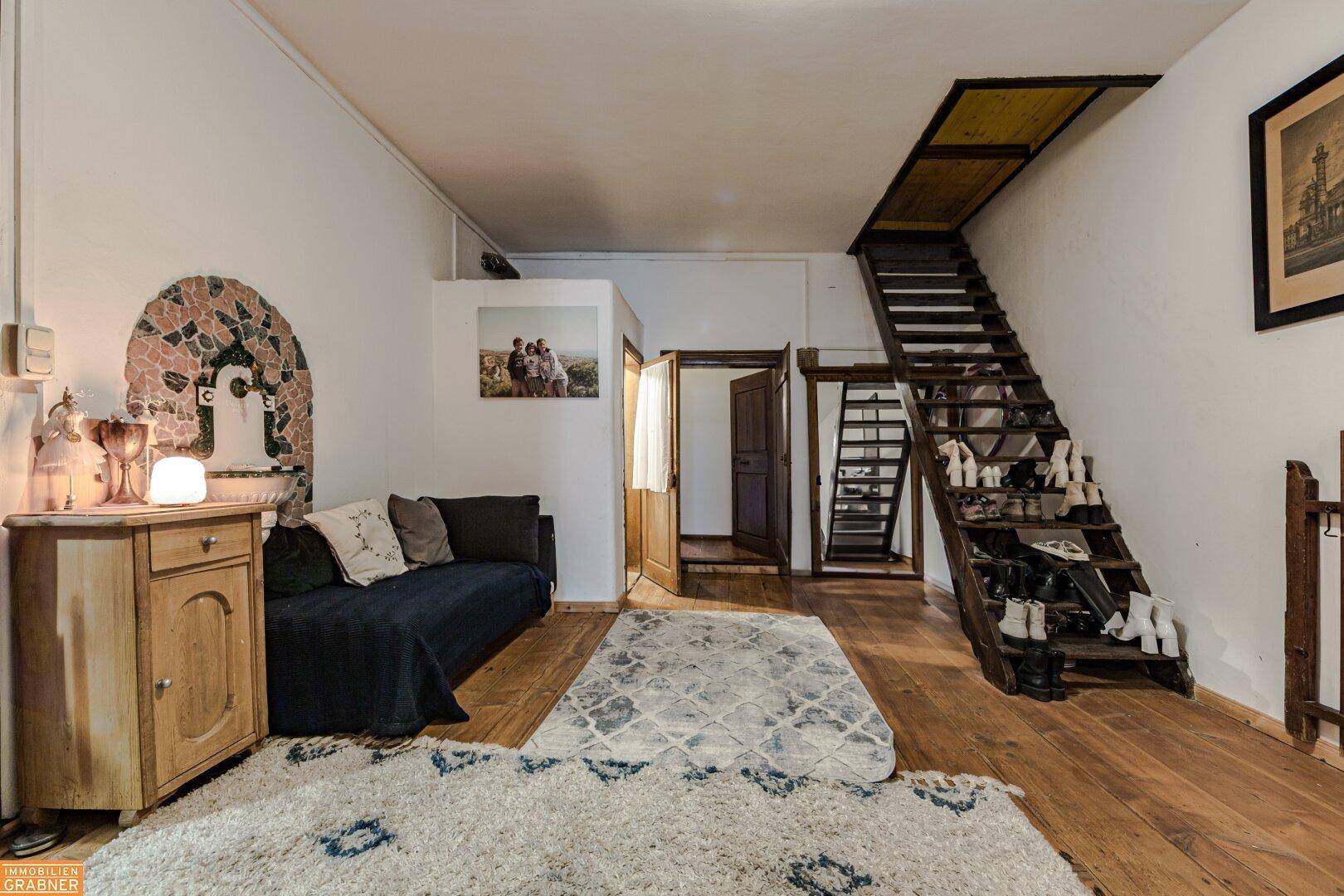 Vielseitiger Raum mit Sofa, Treppe zum Dachboden und rustikalem Wandbrunnen.