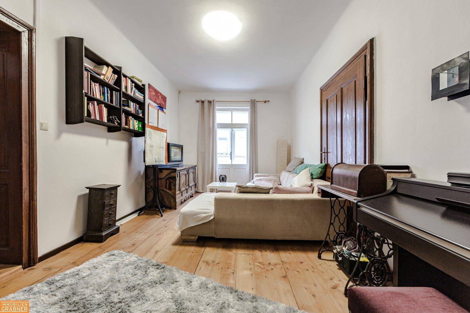 Wohnzimmer mit Holzboden, beigem Sofa, Bücherregal und Klavier, bietet eine gemütliche Atmosphäre.