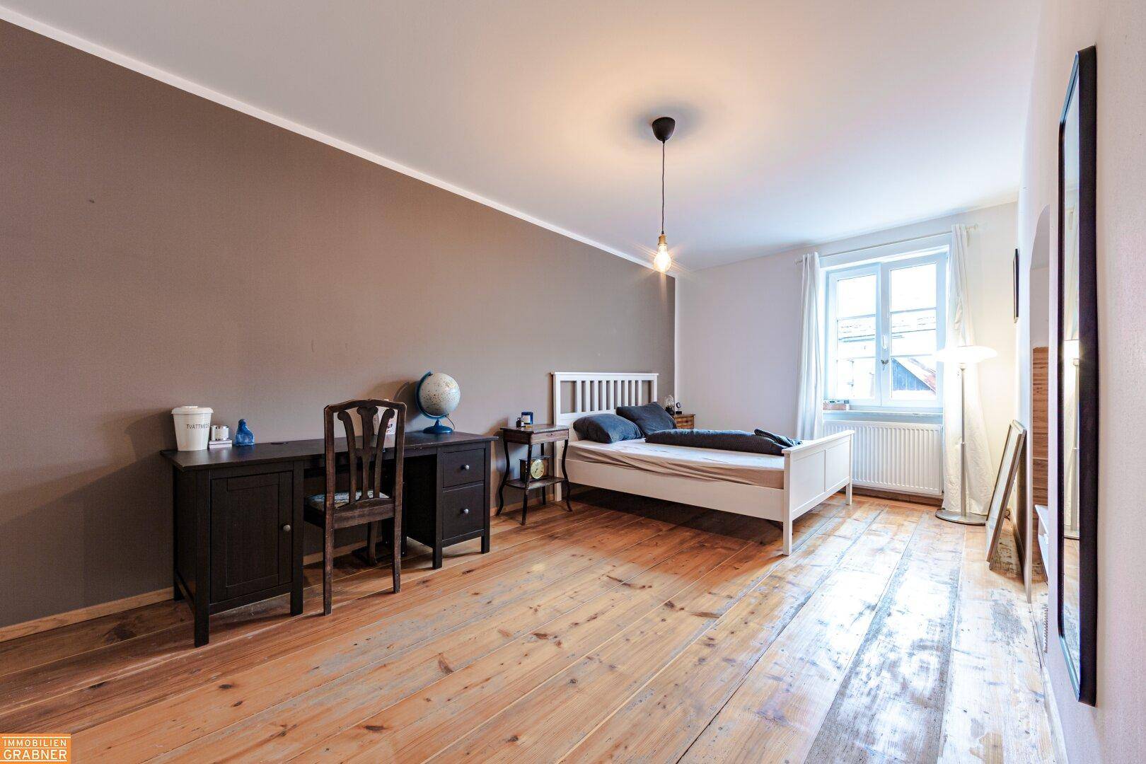 Helles Schlafzimmer mit Holzboden, weißem Bett und Schreibtisch, bietet eine angenehme Wohnatmosphäre.