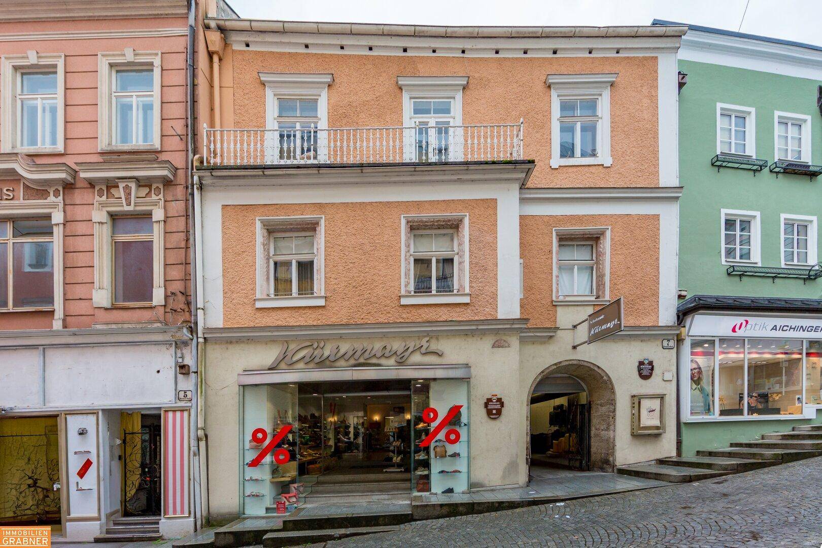 Historisches Gebäude mit Geschäften im Erdgeschoss und Balkon in einer belebten Straße.