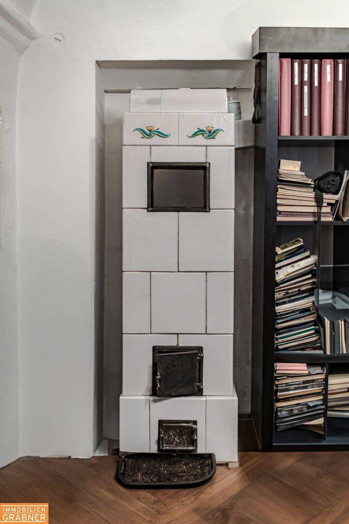 Schmaler weißer Kachelofen neben einem Bücherregal, fügt sich elegant in den Raum ein.