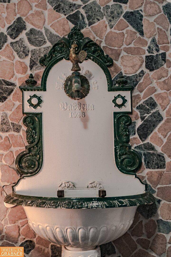 Detailaufnahme eines historischen Wandbrunnens mit grünen Ornamenten und Steinmosaik an der Wand.