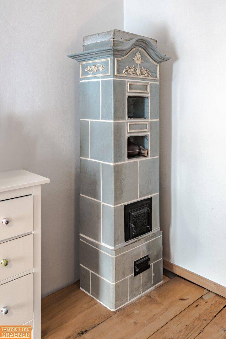 Traditioneller Kachelofen in Grau mit verspielten Details und Holzboden in einem Innenraum.