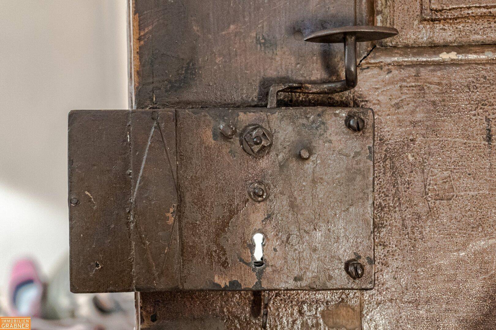 Nahaufnahme eines antiken Türschlosses aus Metall an einer rustikalen Holztür.
