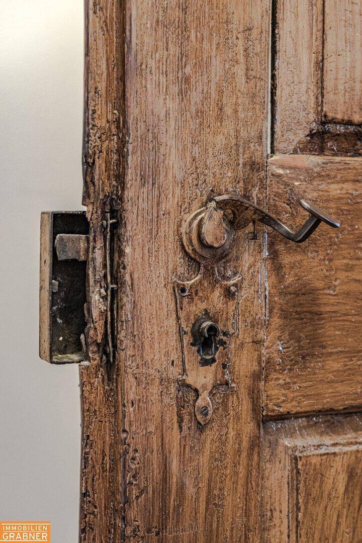 Historische Holztür mit einem kunstvoll verzierten Türgriff und einem robusten Schloss.