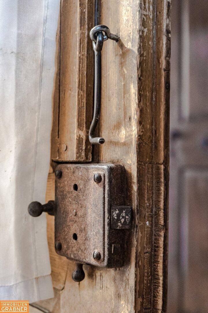 Altes, robustes Türschloss aus Metall mit einem einfachen Hakenverschluss an einer Holztür.