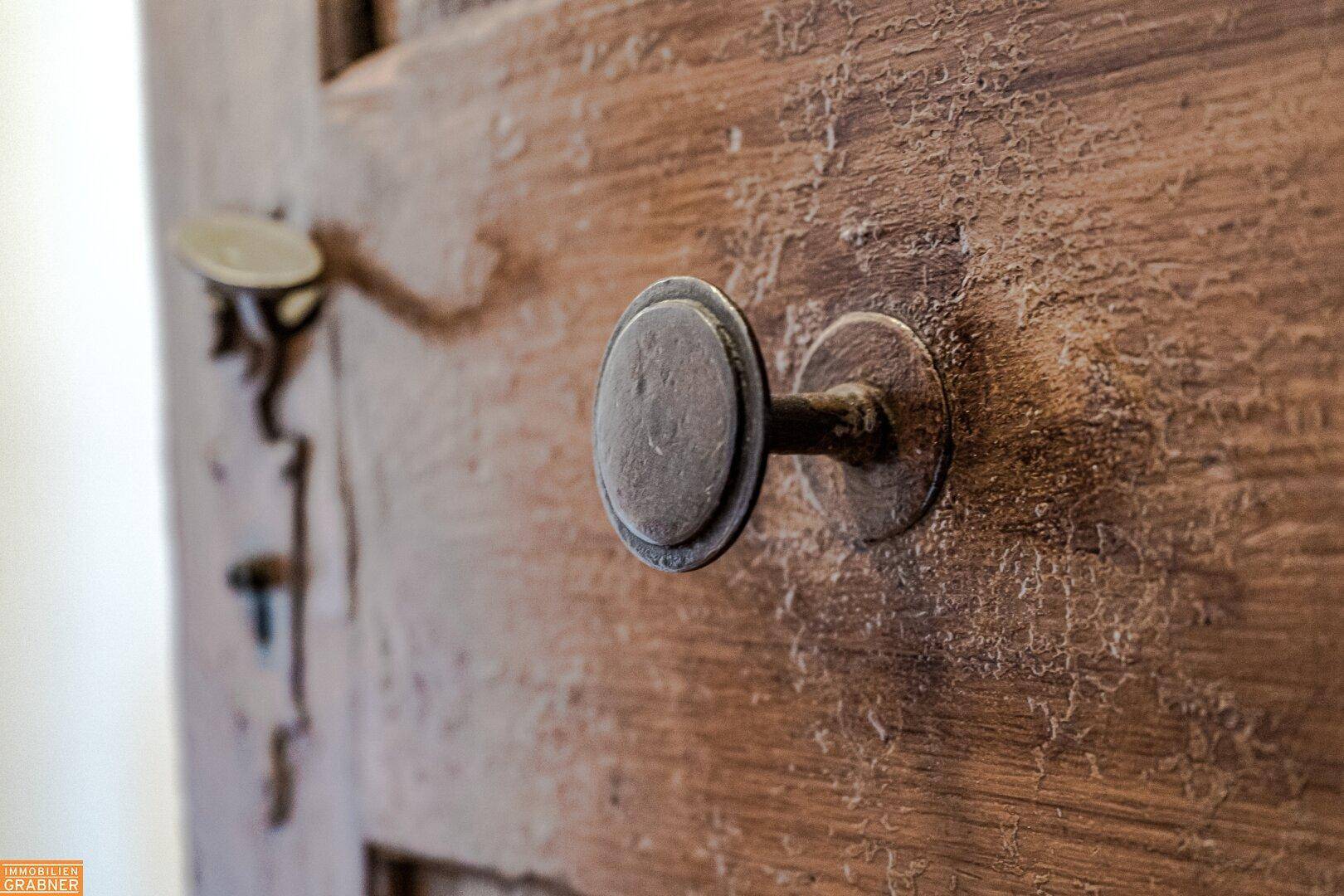 Detailaufnahme eines runden, antiken Türknaufs aus Metall an einer rustikalen Holztür.