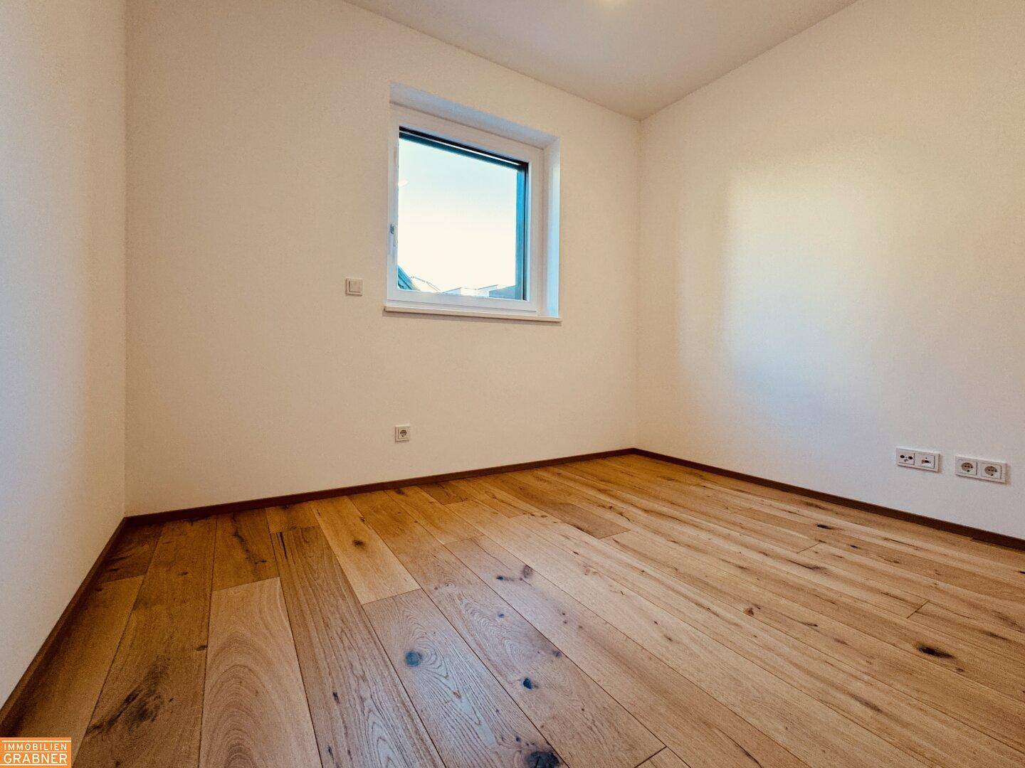 Helles, leeres Zimmer mit Holzboden und einem Fenster, ideal als Schlaf- oder Arbeitszimmer.