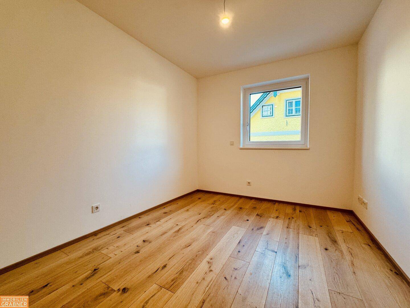 Weiteres helles, leeres Zimmer mit Holzboden und Fenster, bietet vielseitige Nutzungsmöglichkeiten.
