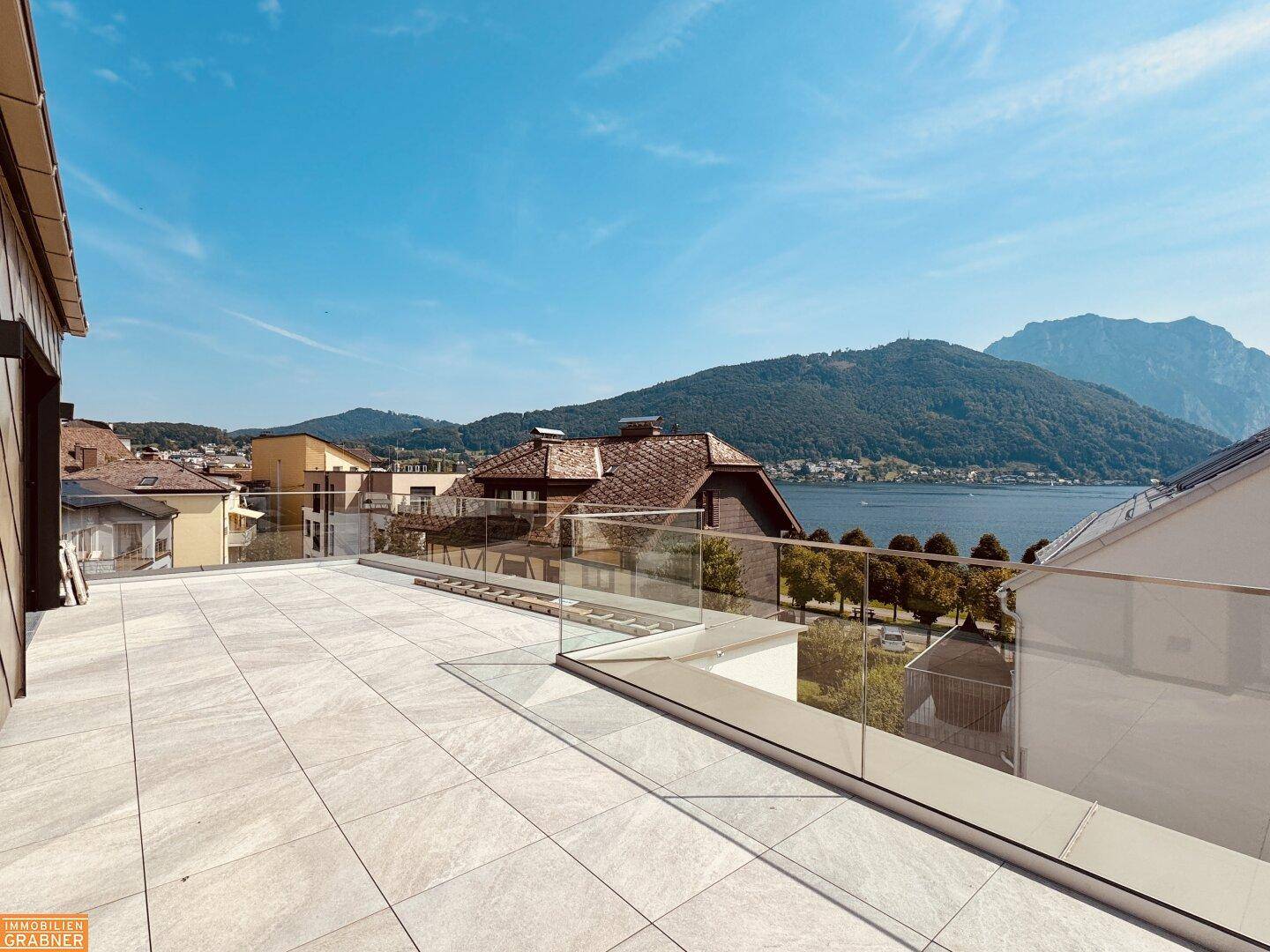 Großzügige Dachterrasse mit Fliesenboden und Glasbrüstung, bietet weiten Blick über Stadt und See.