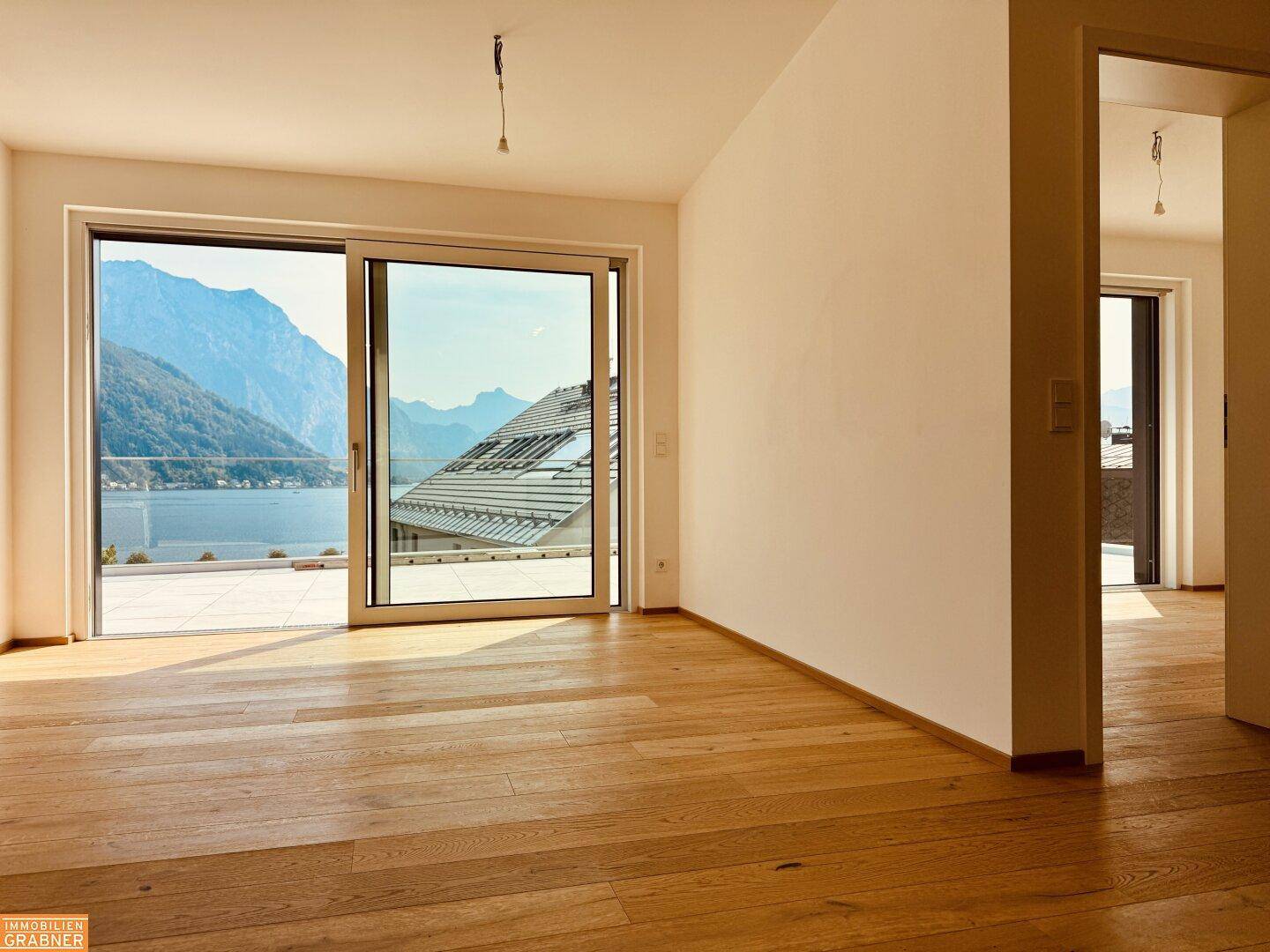 Heller Wohnraum mit Holzboden und großen Schiebetüren, die Zugang zur Terrasse mit Seeblick bieten.