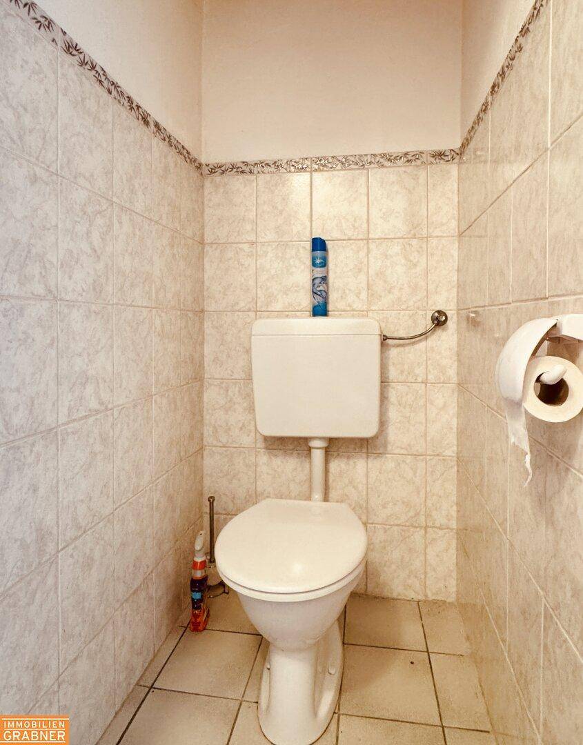 Separate Toilette mit hellen Fliesen an Wänden und Boden, sauber und funktional.