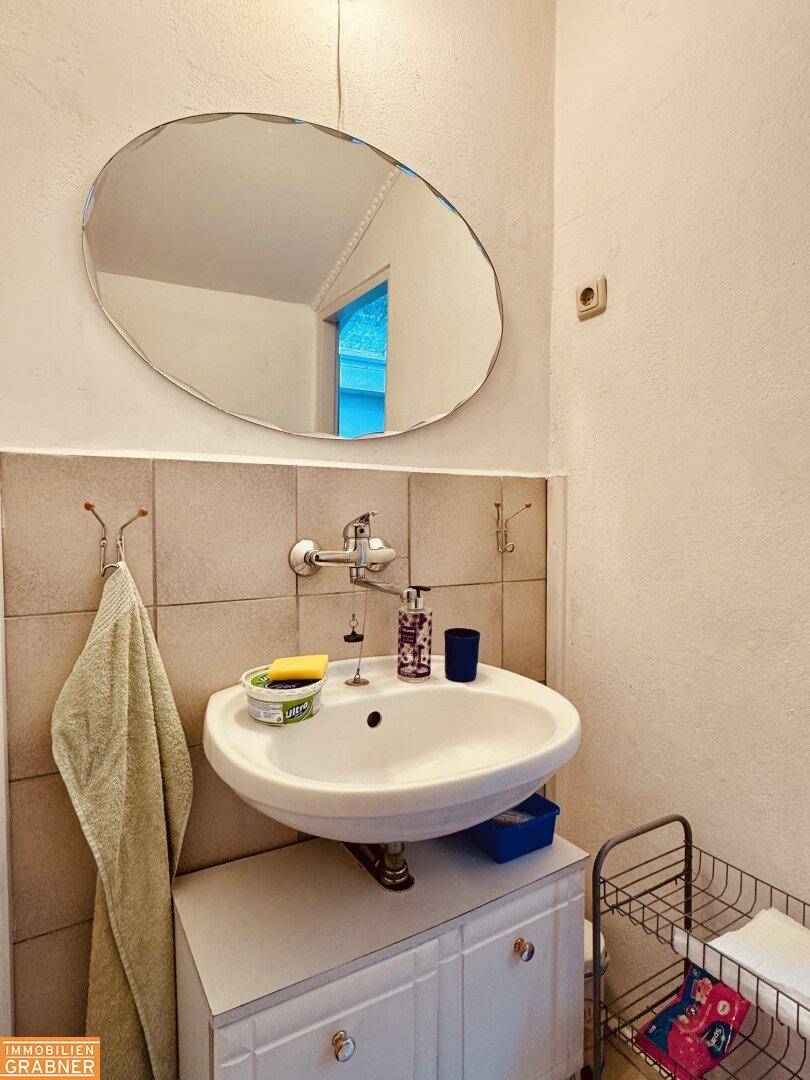 Badezimmer mit Waschbecken, ovalem Spiegel und hellen Fliesen, funktional eingerichtet.