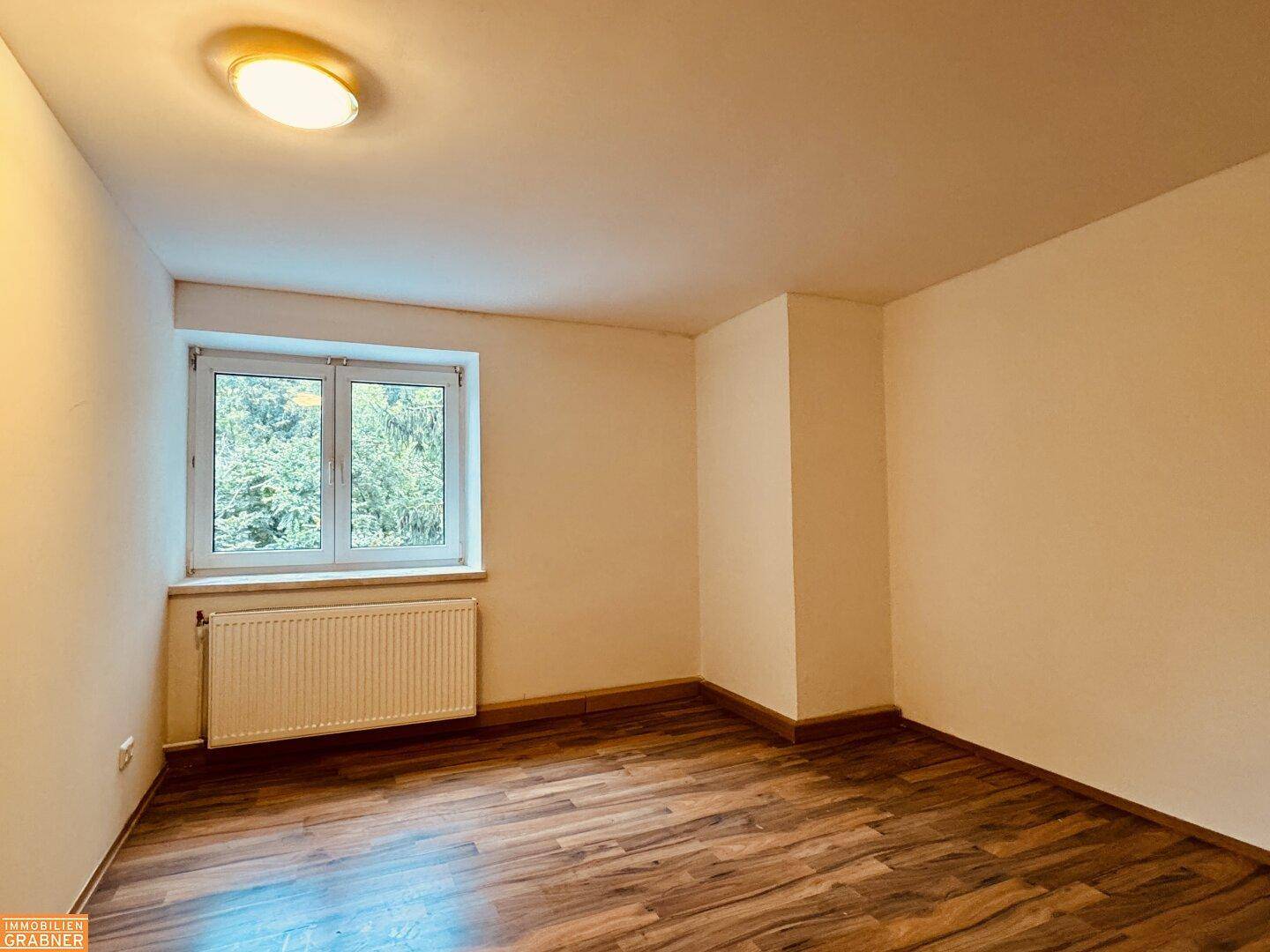 Gemütliches Schlafzimmer mit Holzboden, Fenster und Heizkörper, bietet einen ruhigen Rückzugsort.