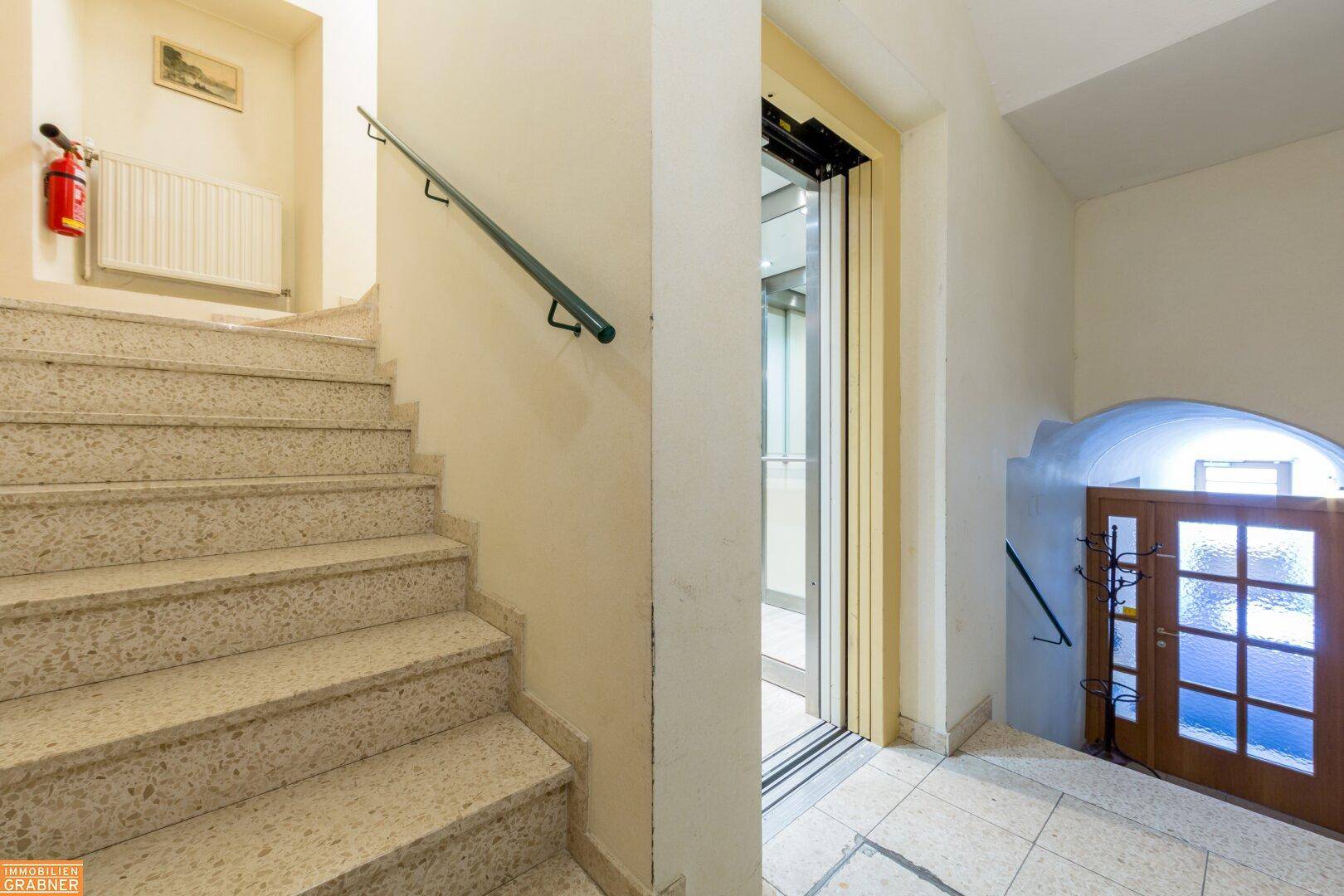 Treppenhaus mit Steinstufen und modernem Aufzug für bequemen Zugang zu den Etagen.