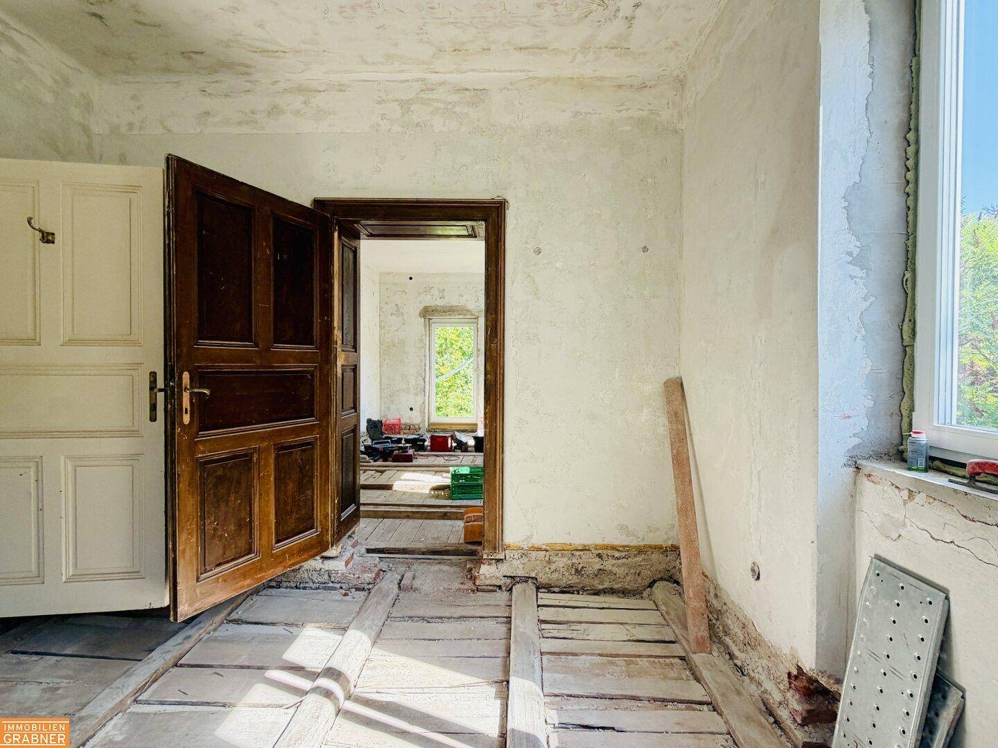 Innenraum in Renovierung mit freigelegten Holzdielen und originalen Holztüren.