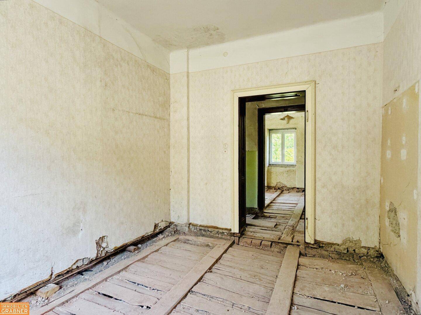 Unmöblierter Raum mit abgenutzten Wänden und freiliegenden Holzdielen, bereit für die Renovierung.