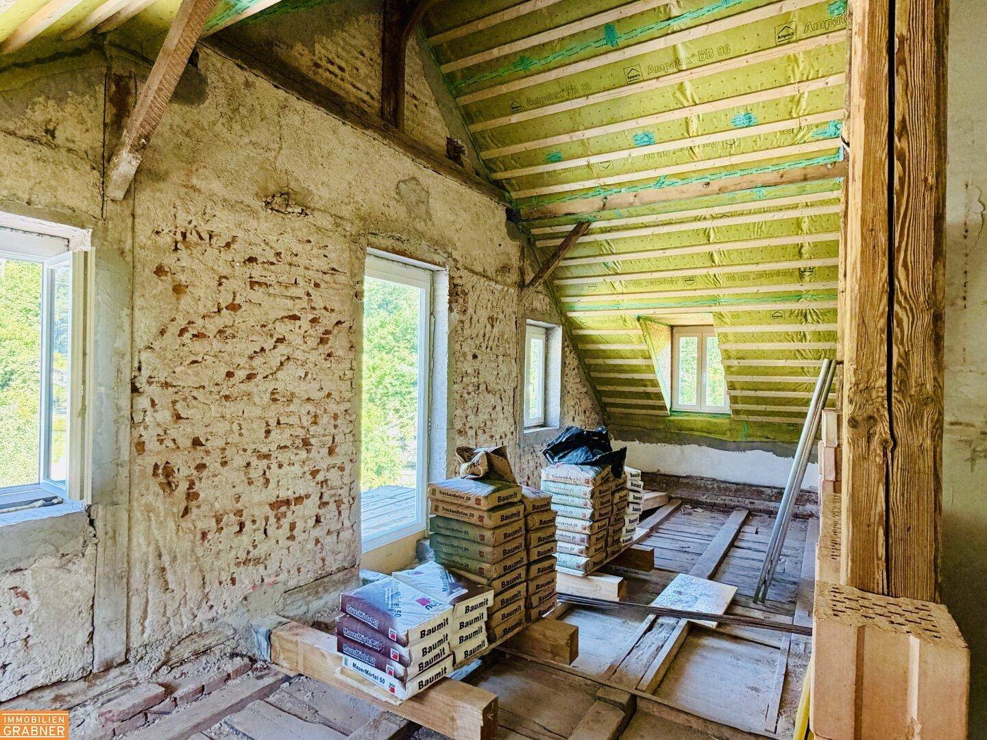 Dachgeschoss im Rohbau mit unverputzten Wänden, Holzbalken und Baumaterialien, bereit zur Fertigstellung.