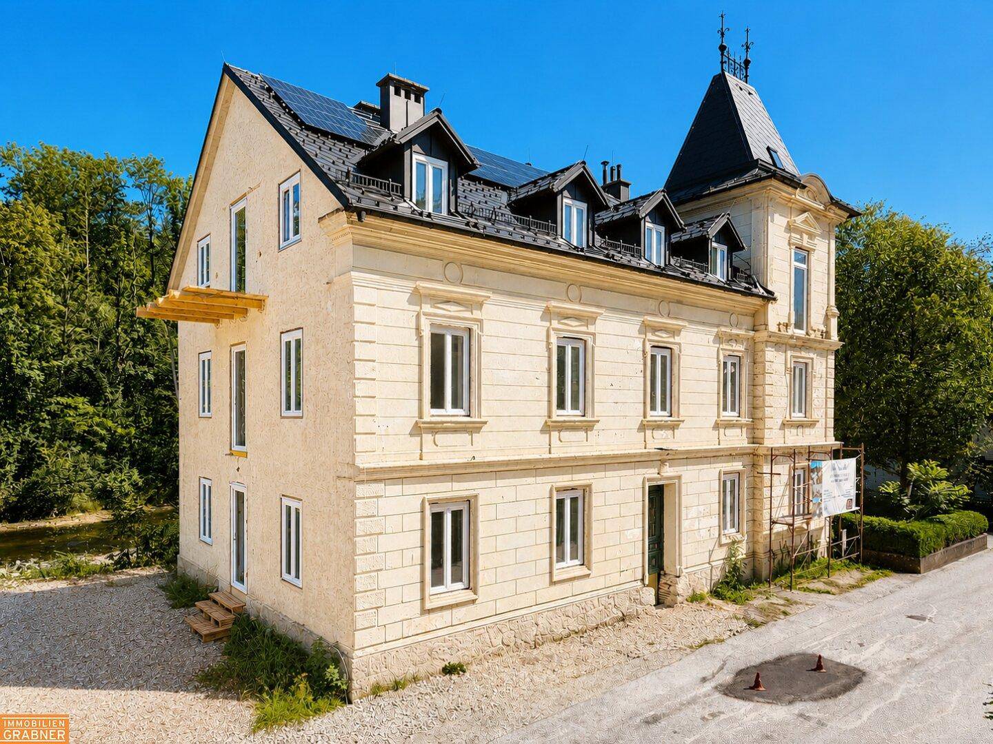 Historische Villa mit eleganter Fassade, modernen Solarpaneelen auf dem Dach und umliegender Natur.
