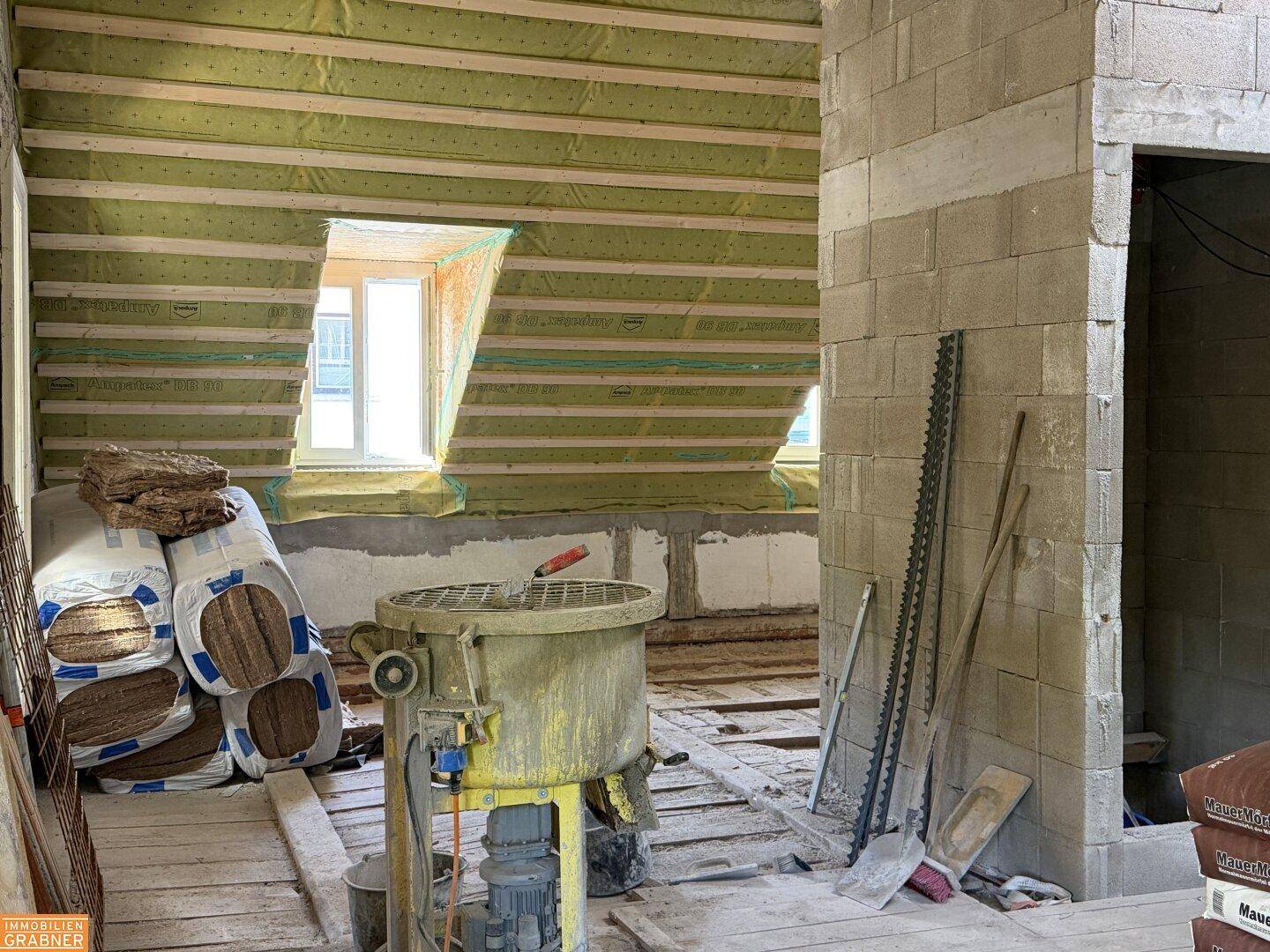 Dachgeschoss im Rohbau mit sichtbarer Dämmung, Holzbalken und Baumaterialien.