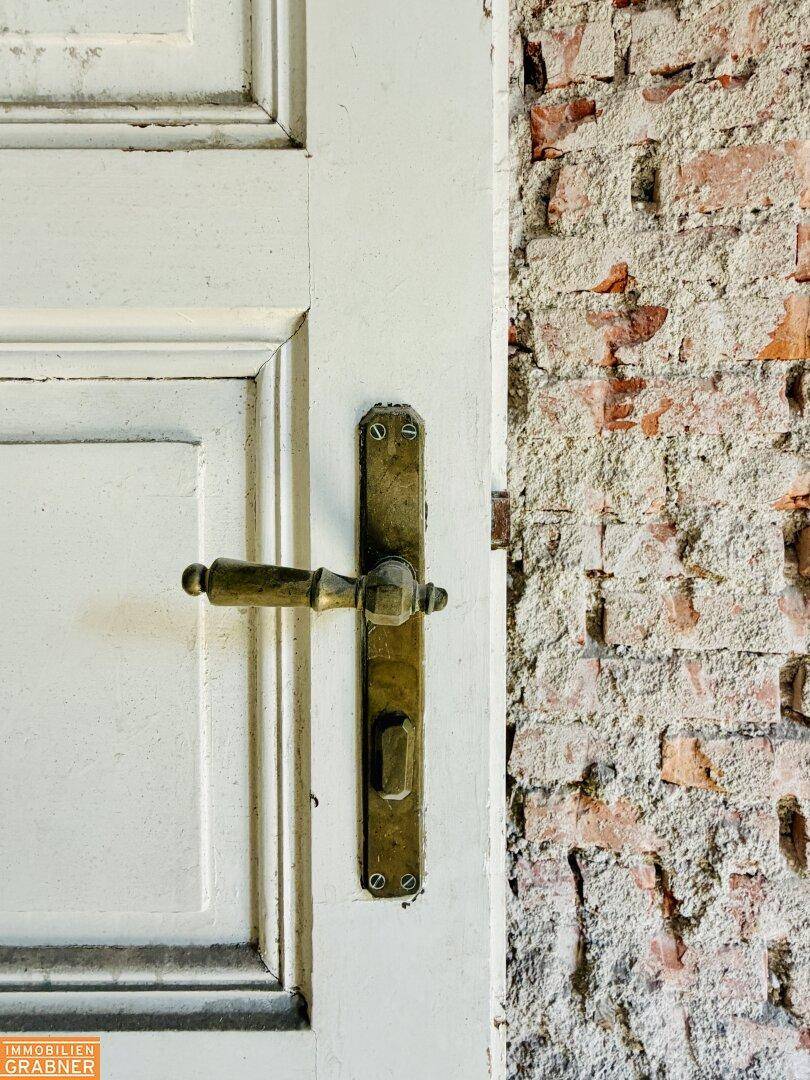 Nahaufnahme einer alten weißen Holztür mit Messinggriff neben einer unverputzten Ziegelwand.