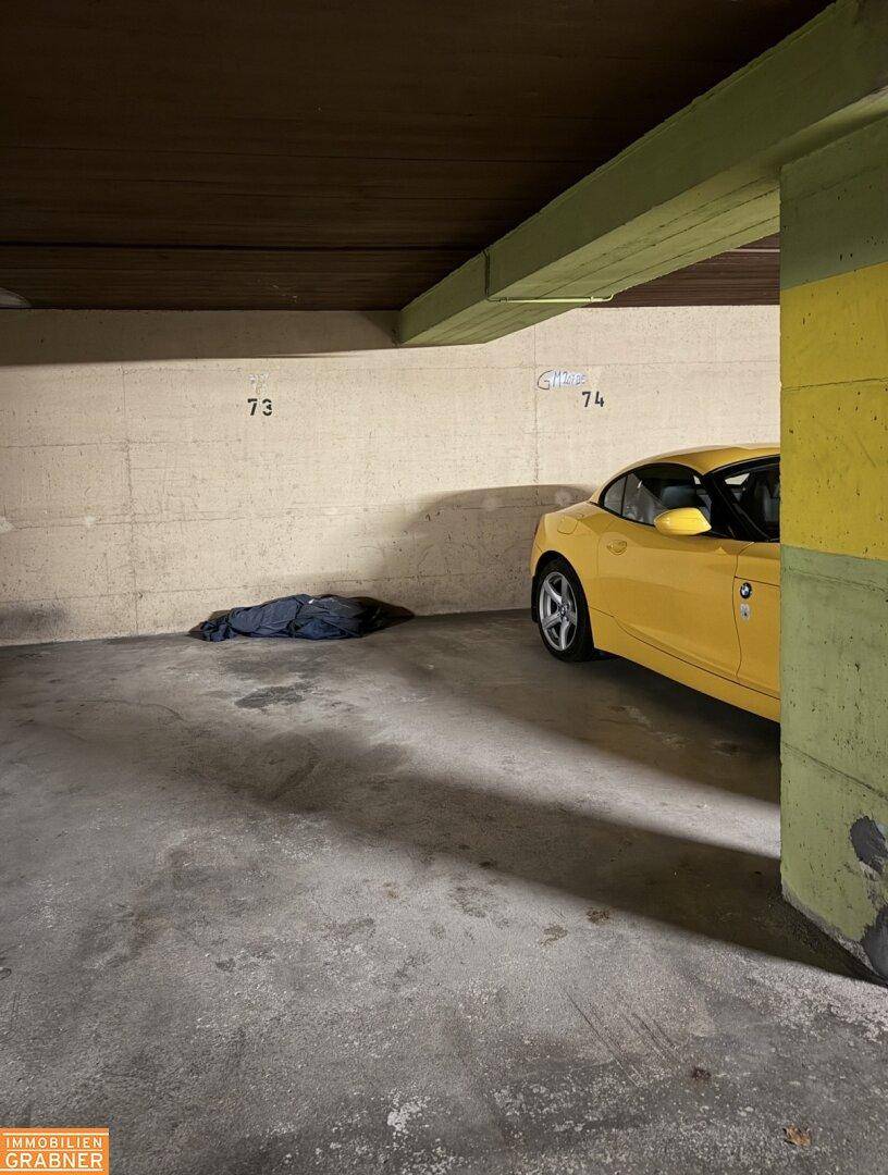Tiefgaragenstellplatz mit Betonwänden und einem geparkten gelben Fahrzeug.