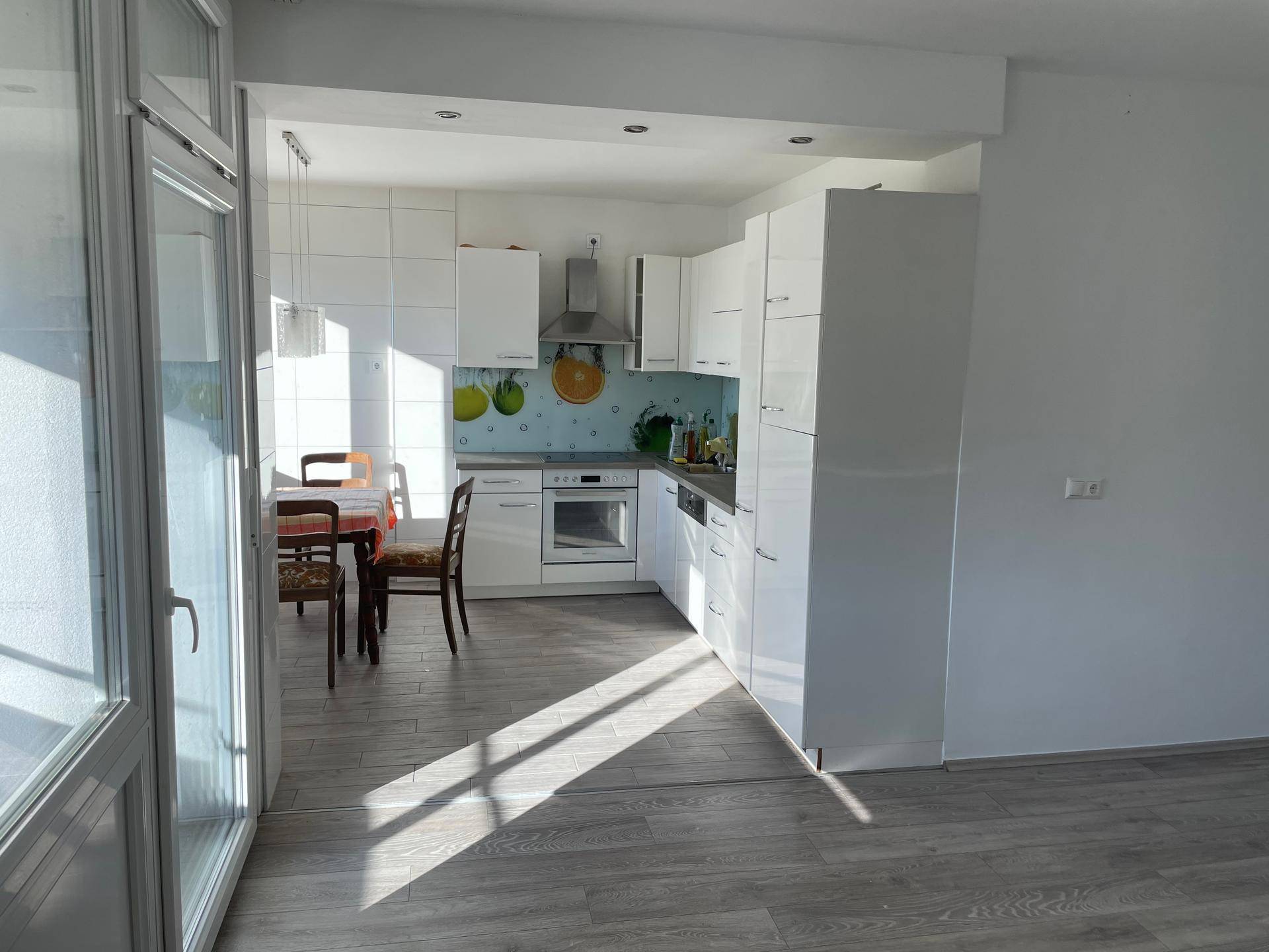 Moderne, offene Küche mit weißen Hochglanzfronten, Essbereich und viel Tageslicht.