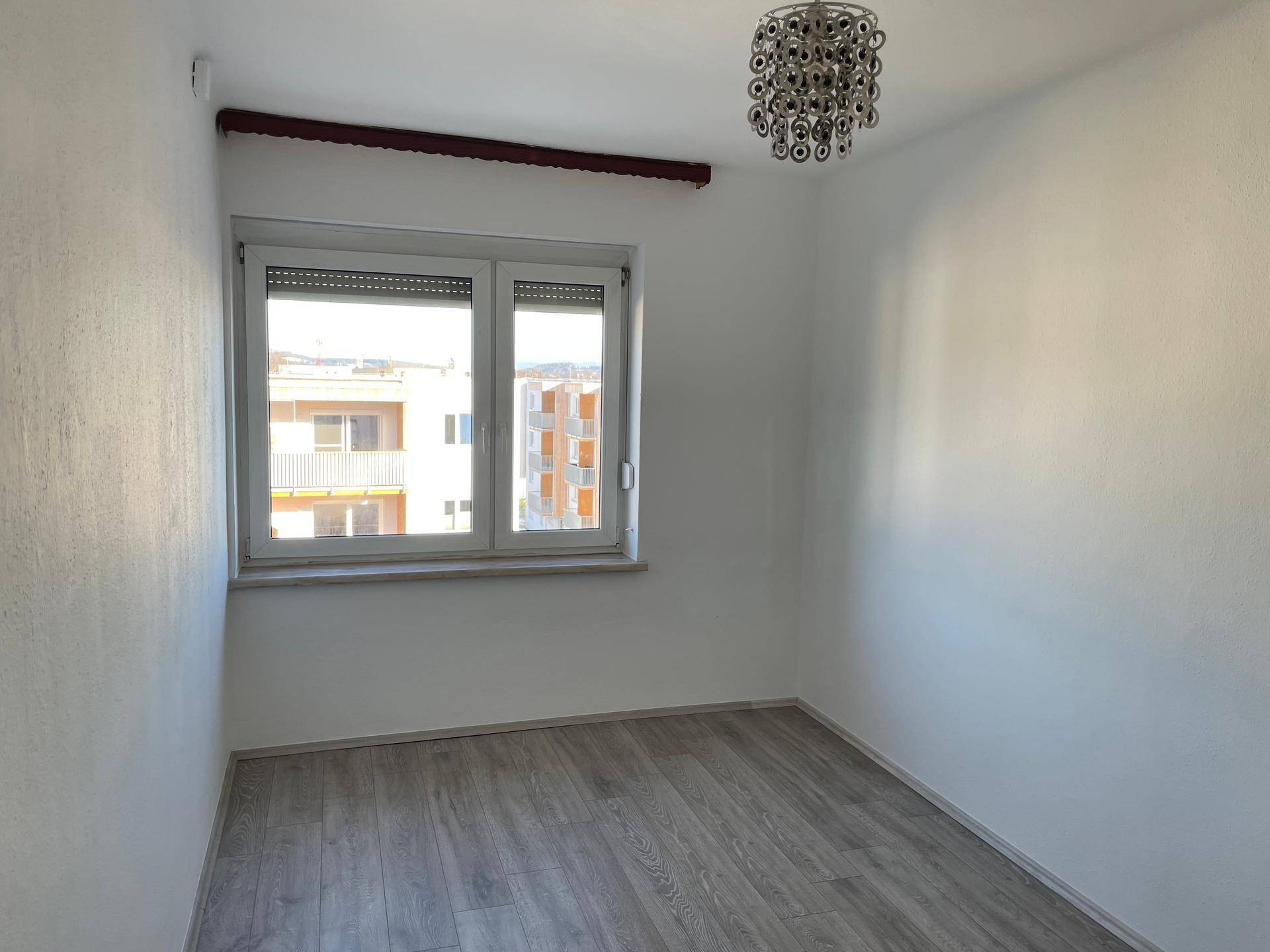 Helles Kinderzimmer mit Laminatboden, weißen Wänden und einem Fenster mit Blick nach draußen.