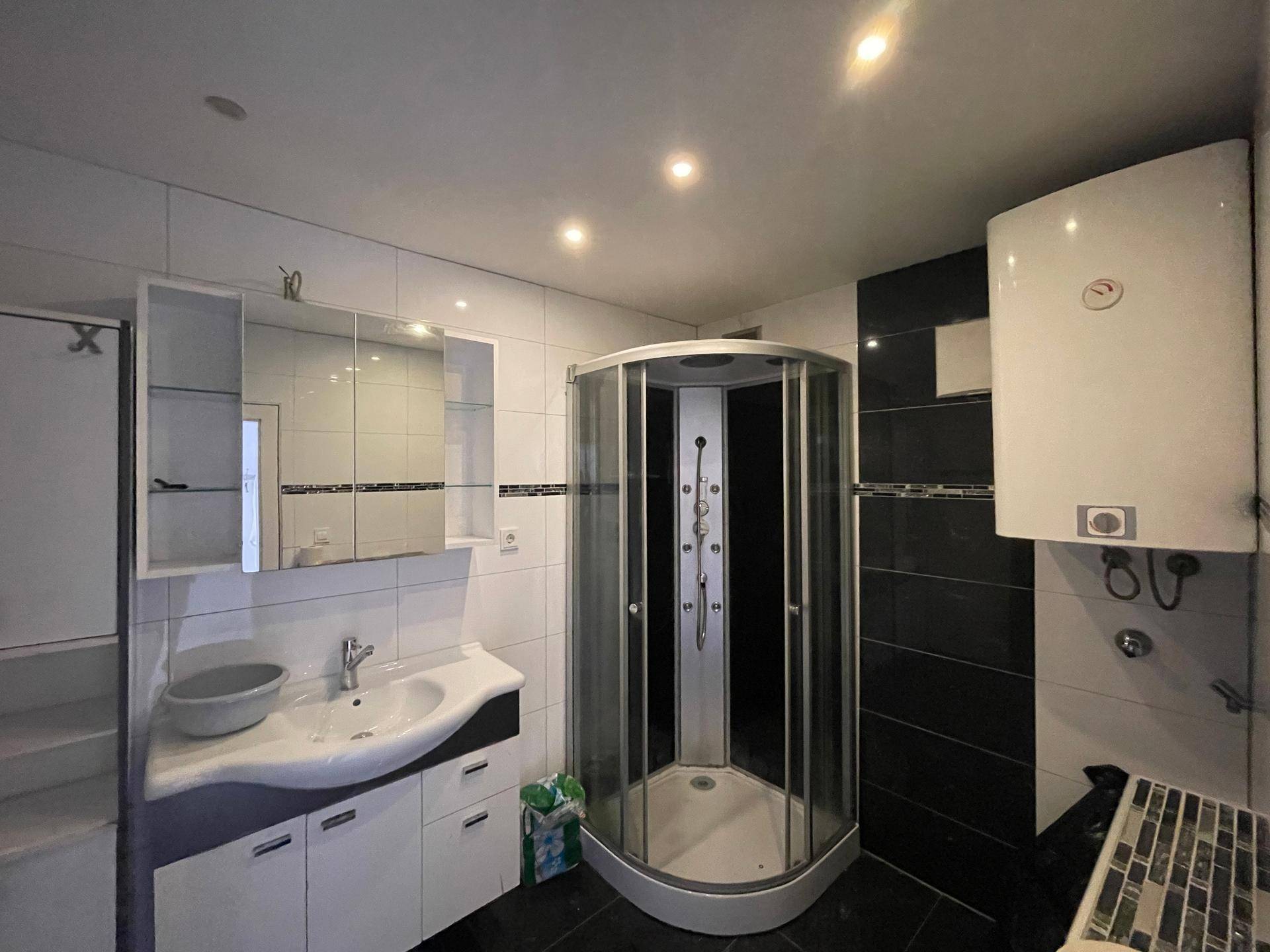 Modernes Badezimmer mit schwarz-weißen Fliesen, Duschkabine und Waschtisch mit Spiegelschrank.
