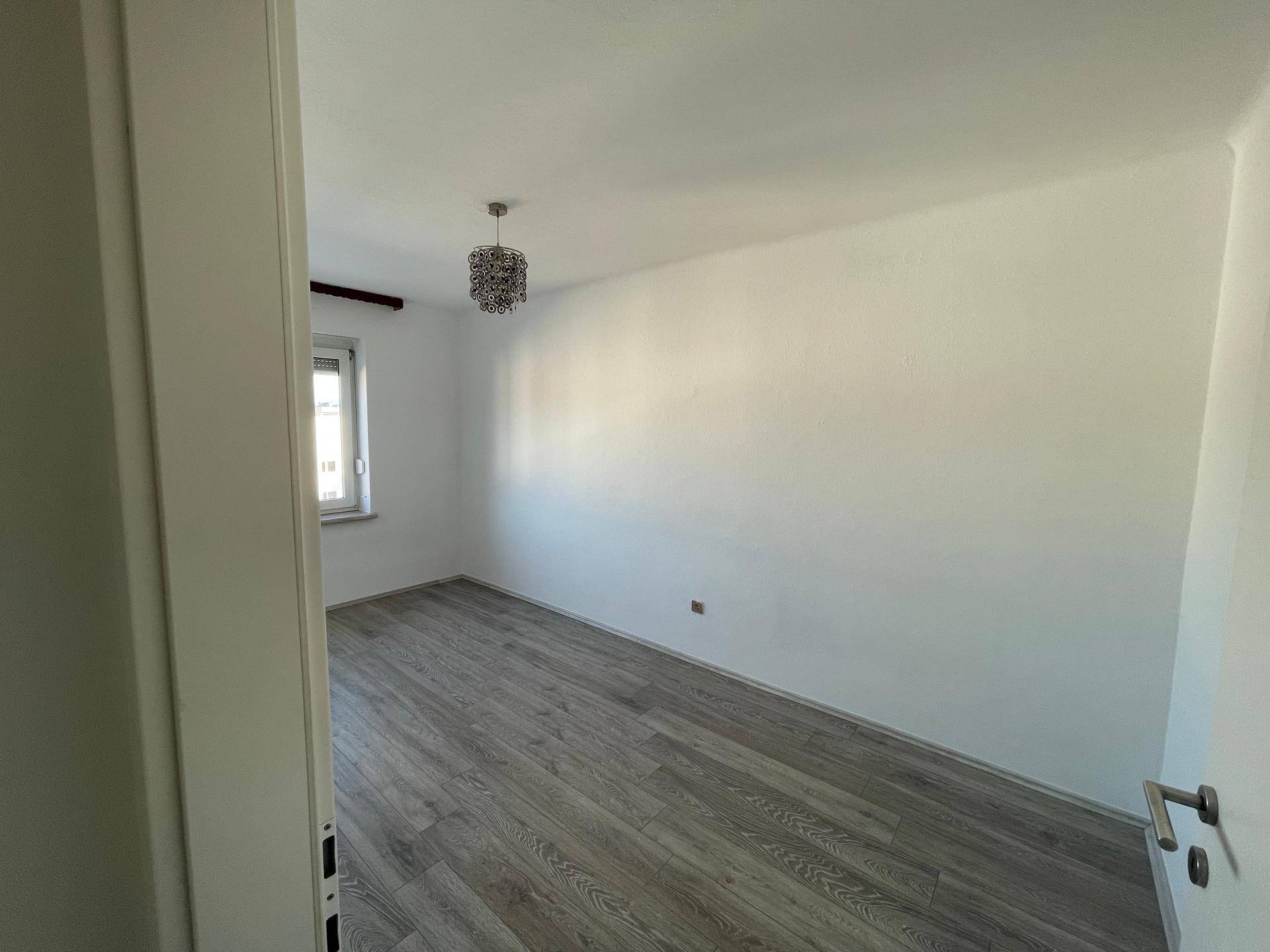 Blick in ein helles Zimmer mit Laminatboden und einem Fenster, ideal als Kinder- oder Arbeitszimmer.
