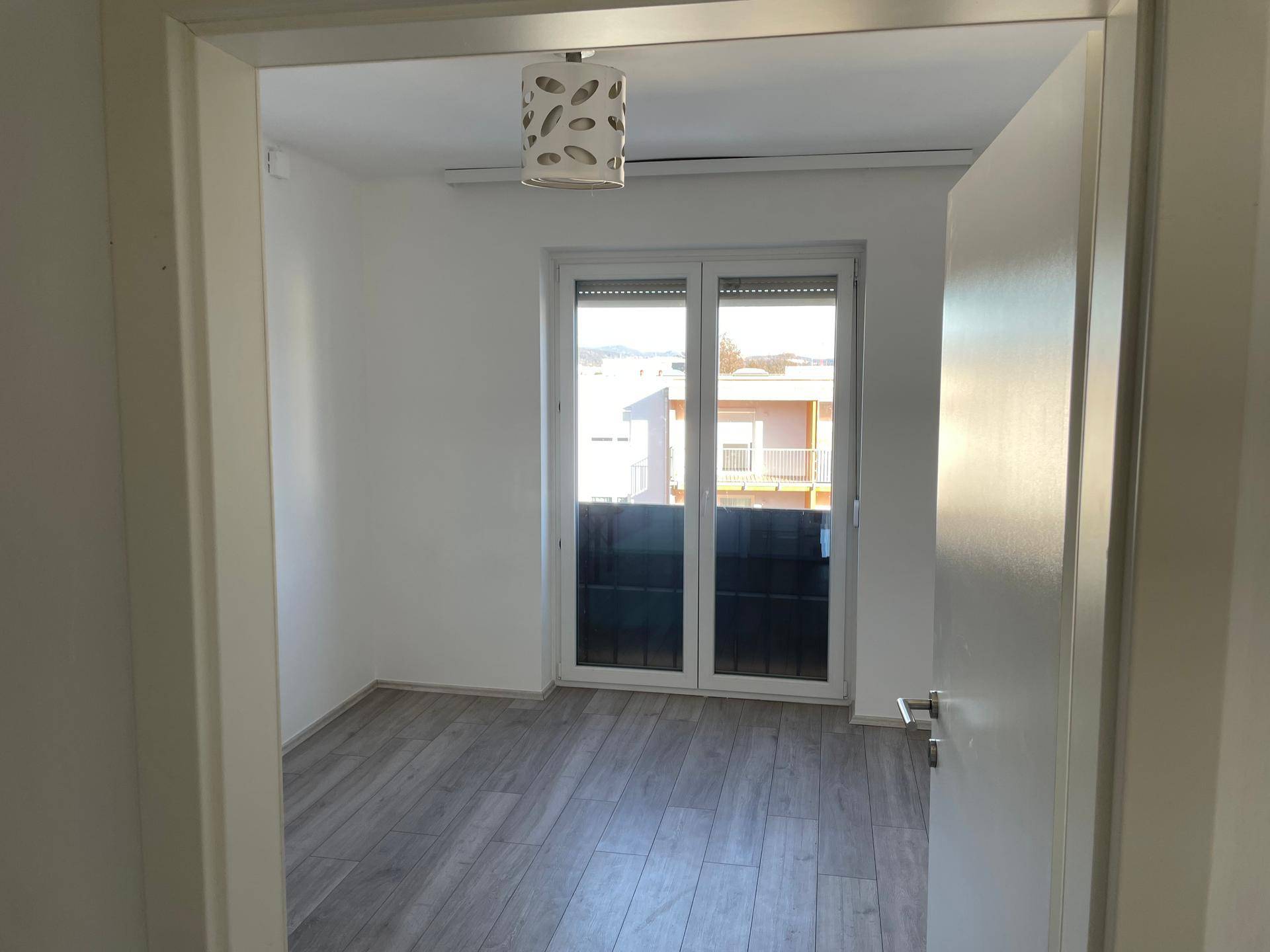Blick in ein helles Schlafzimmer mit Laminatboden und direktem Zugang zu einem Balkon.