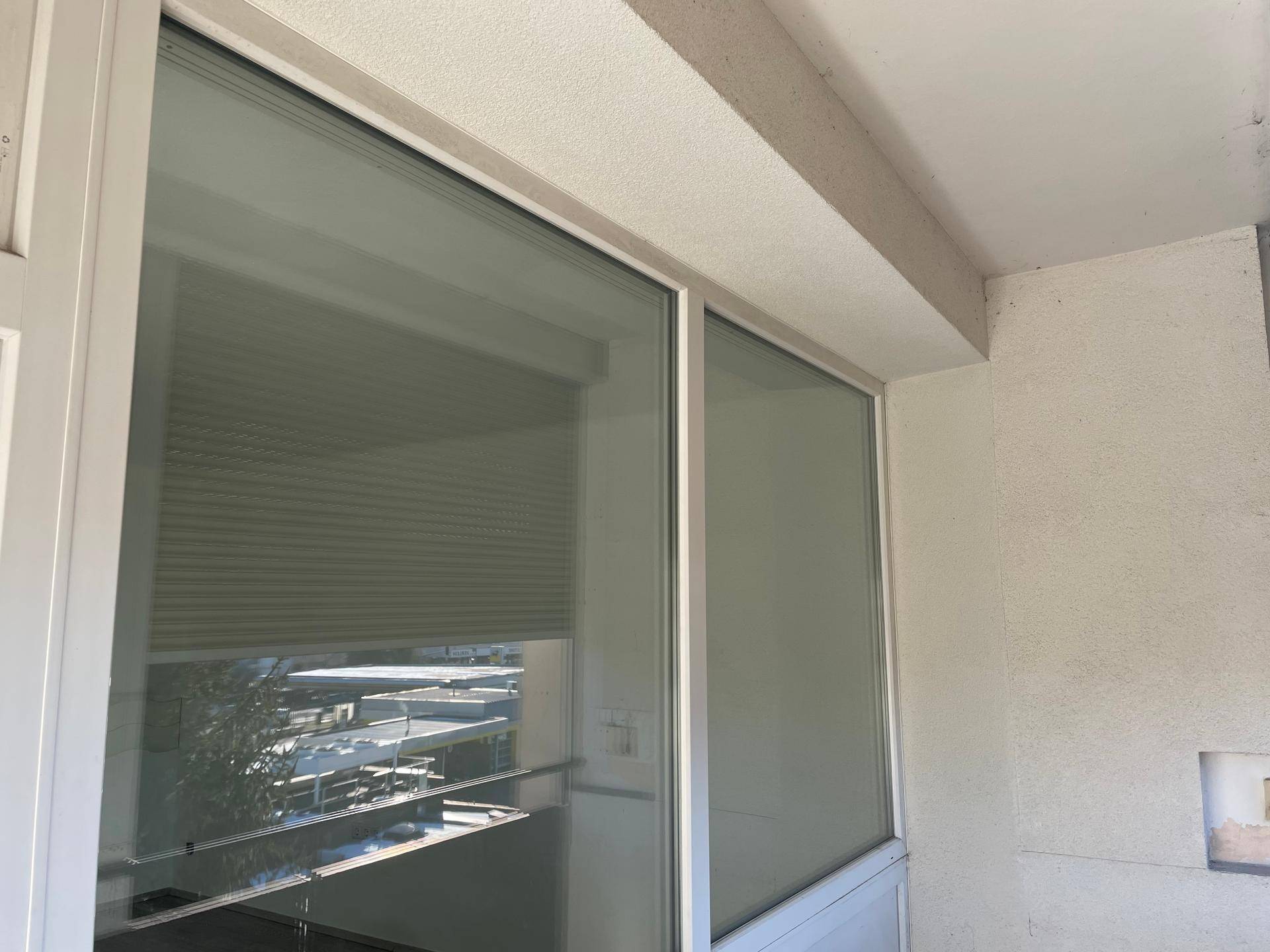 Detailansicht des Balkons mit Rollladen und der strukturierten Außenwand des Gebäudes.